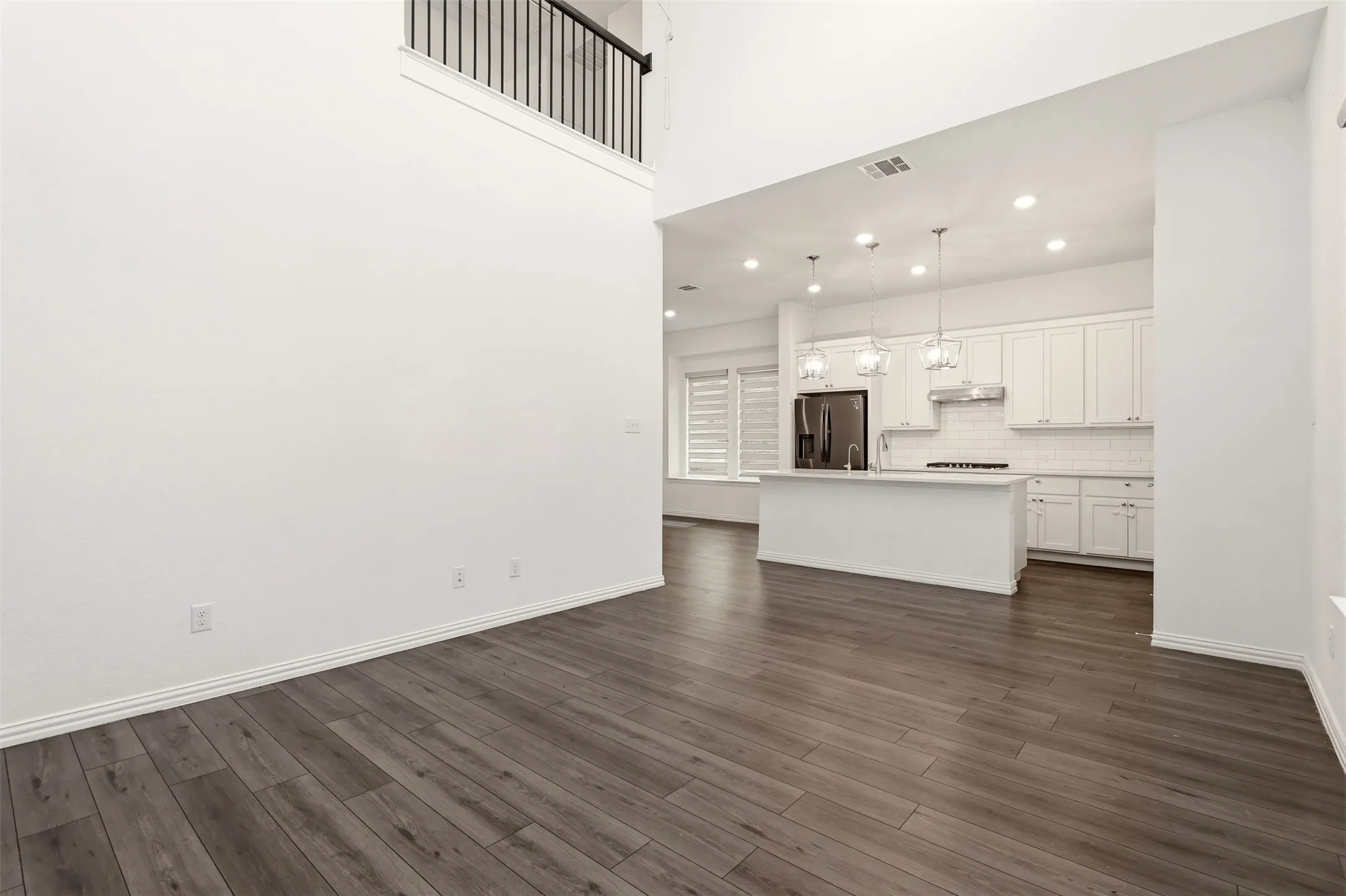 Open-concept kitchen and living area featuring wood-finish flooring, recessed lighting, and a second-story balcony with metal railing