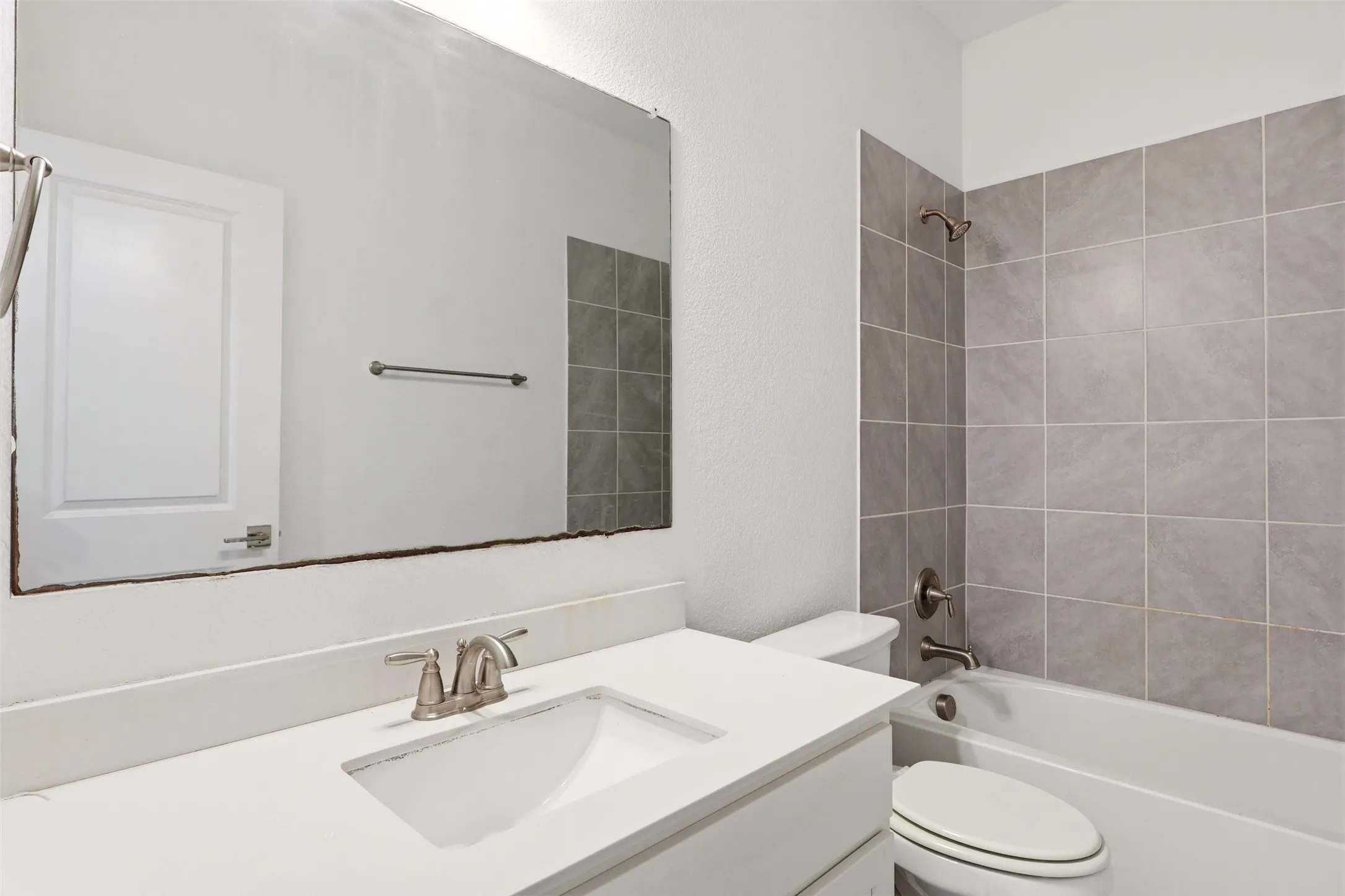 Bathroom featuring a white vanity with an integrated sink, brushed nickel faucet, a large wall-mounted mirror, and a full-size bathtub with subway tile surround