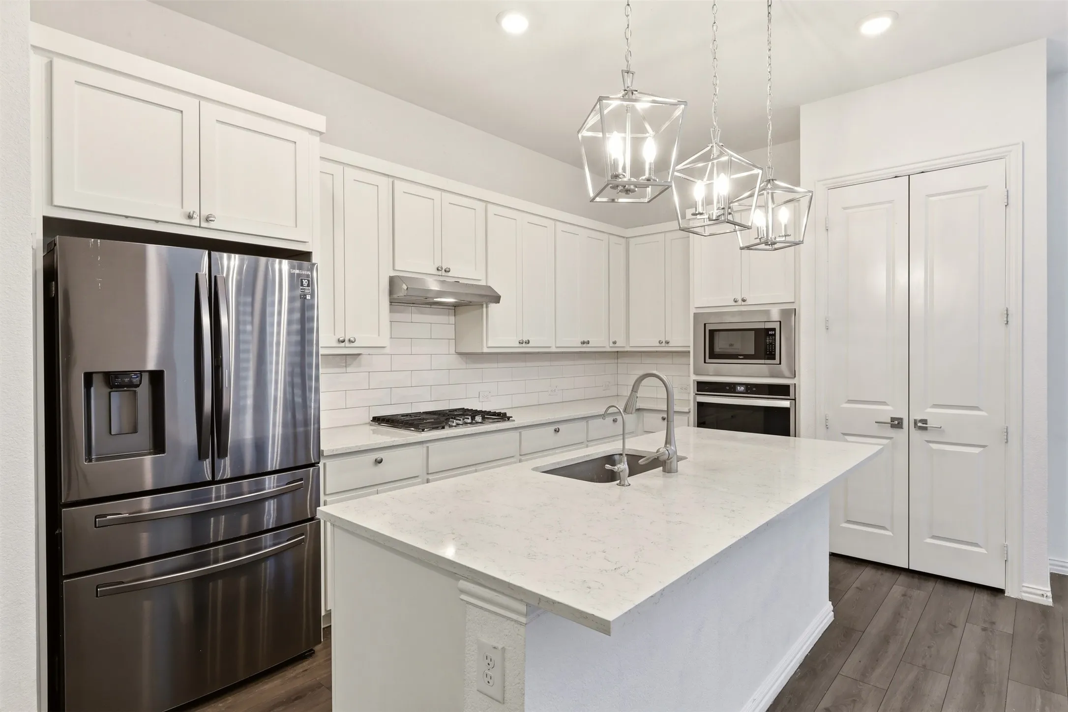 Kitchen featuring white shaker-style cabinetry, a large center island with a sink, stainless steel appliances, a subway tile backsplash, and dark wood-finish flooring