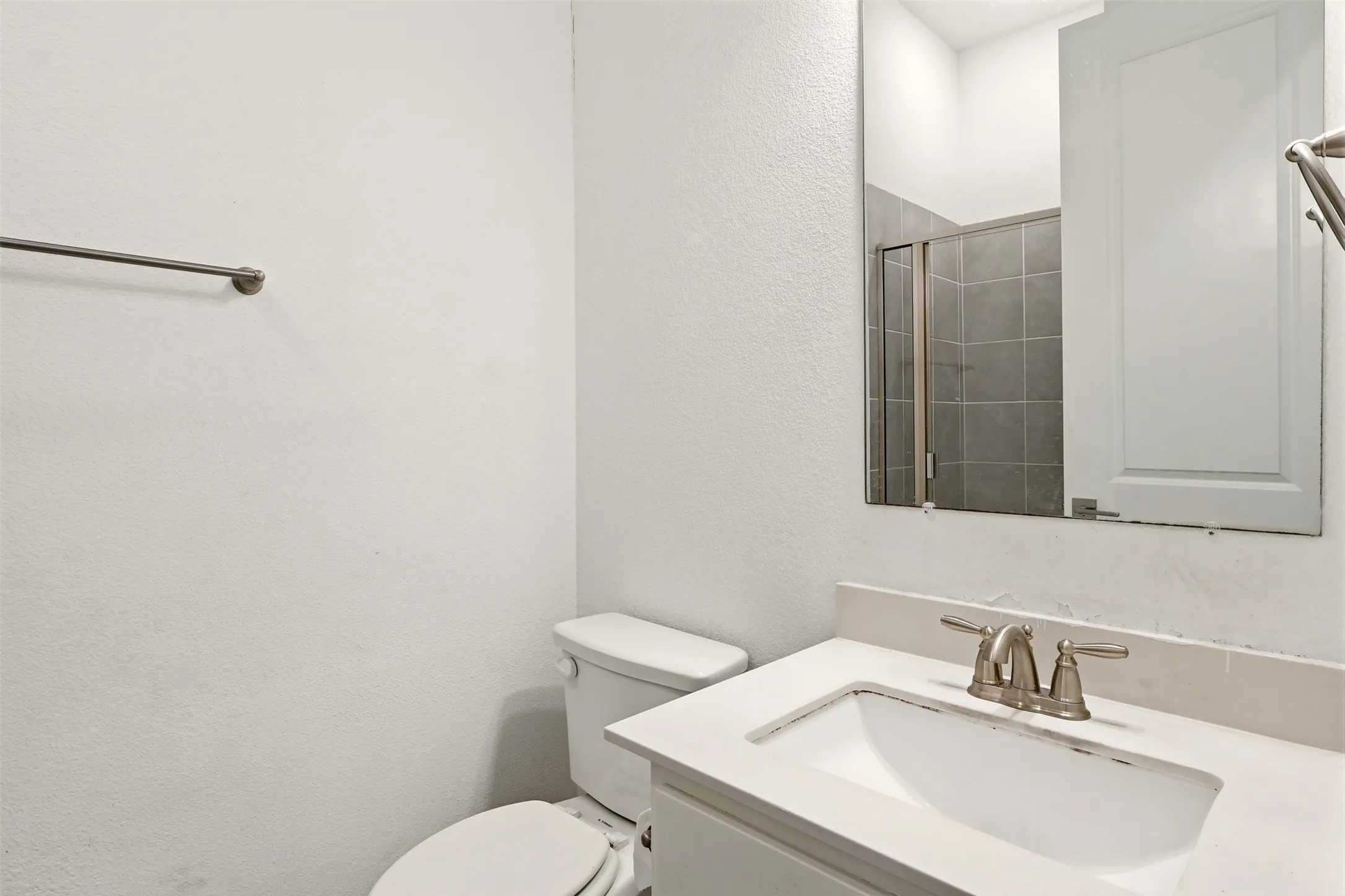 Bathroom featuring a white vanity with an integrated sink, brushed nickel faucet, large mirror, and a toilet