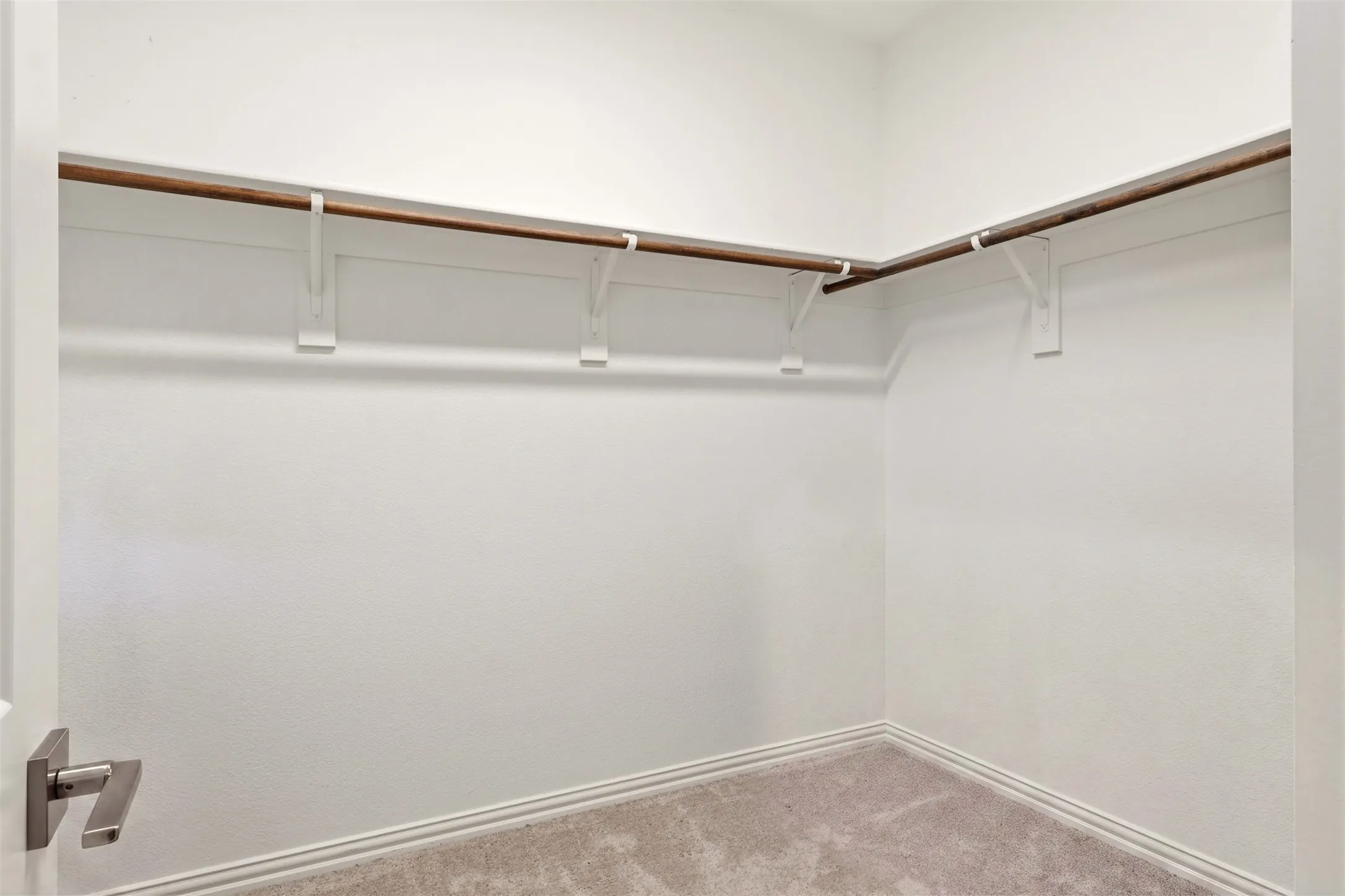 Walk-in closet with light gray carpeting, white walls, and a multi-level clothing rod system