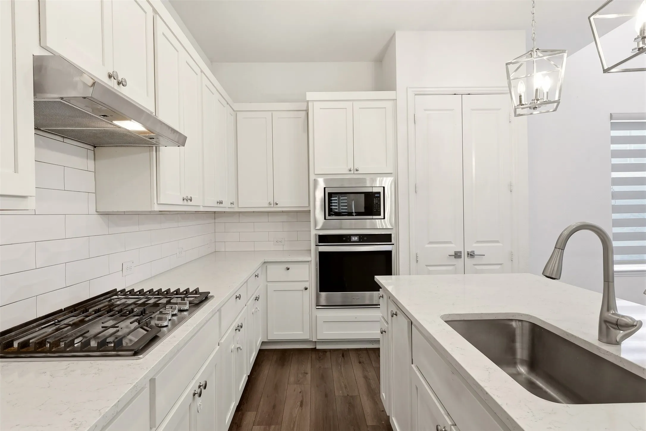 White shaker cabinetry, light-toned countertops, and wood-finish flooring define this kitchen