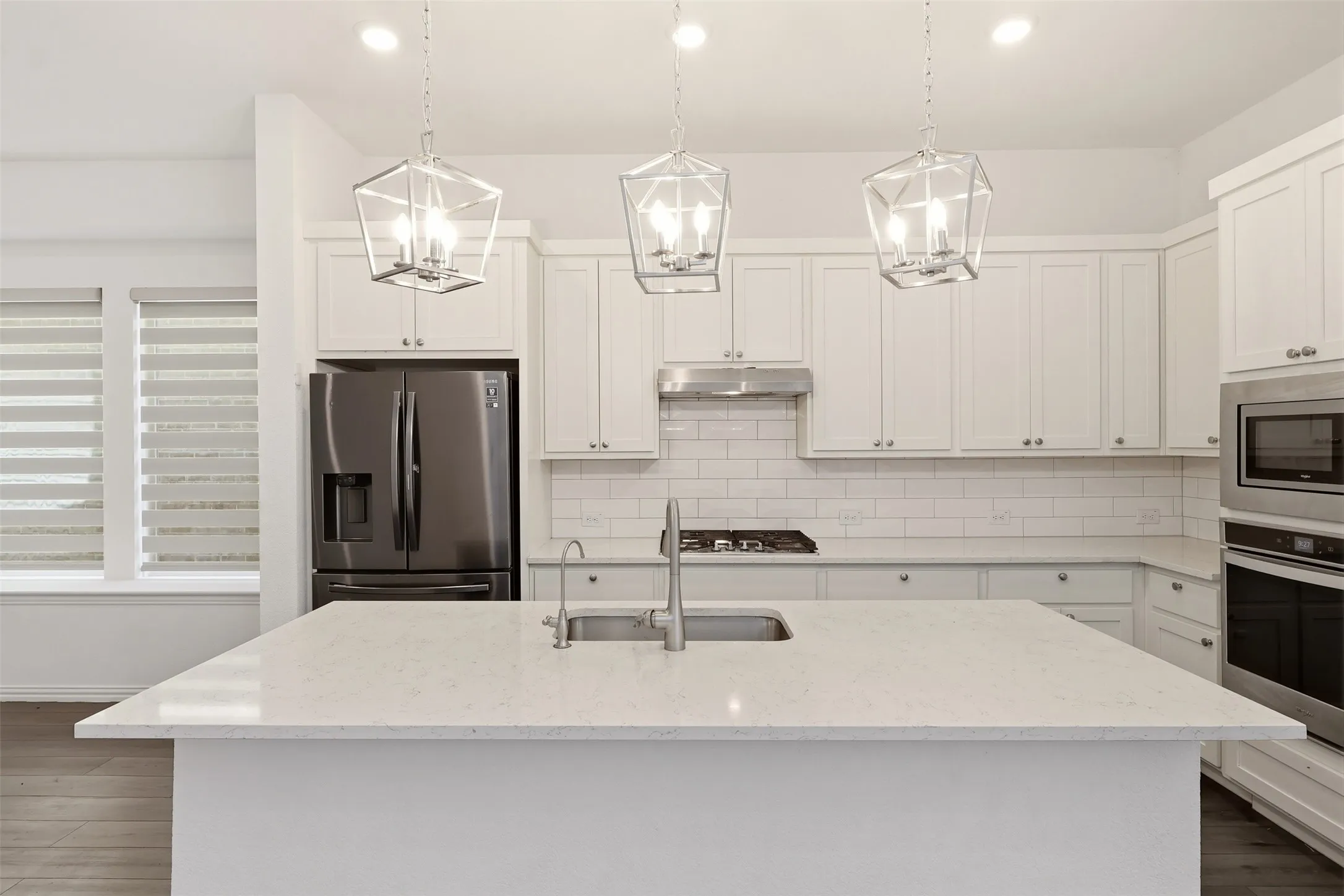Kitchen featuring a large central island with an undermount sink, white shaker cabinetry, stainless steel appliances, a subway tile backsplash, and wood-finish flooring