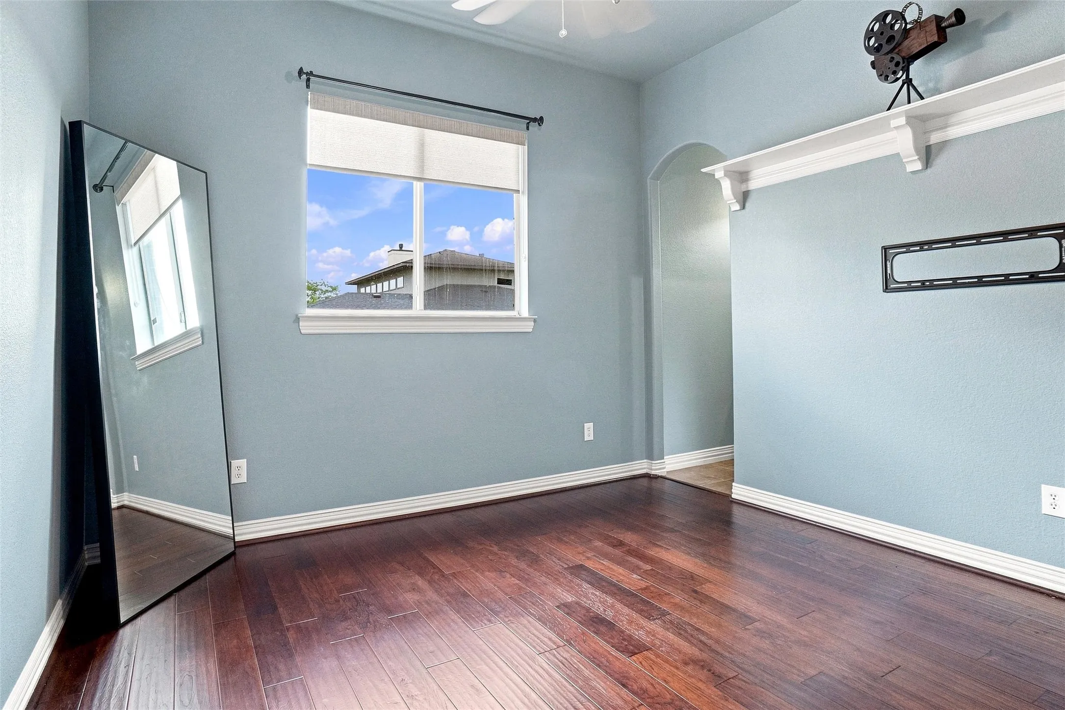 Rich wood-finish flooring throughout, complemented by a prominent window with a roller shade