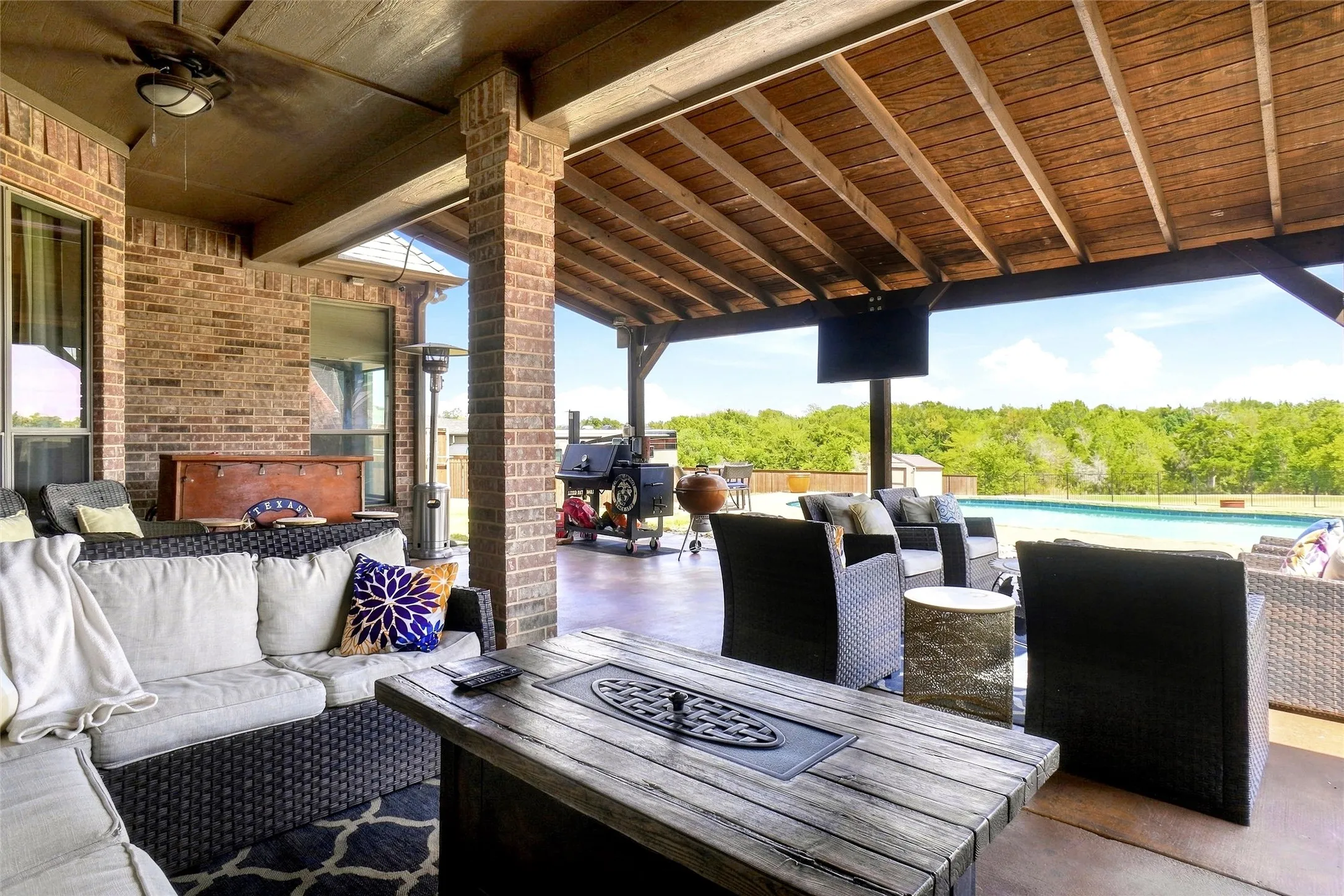 Expansive covered patio featuring a wood-plank ceiling, exposed beams, and brick support columns