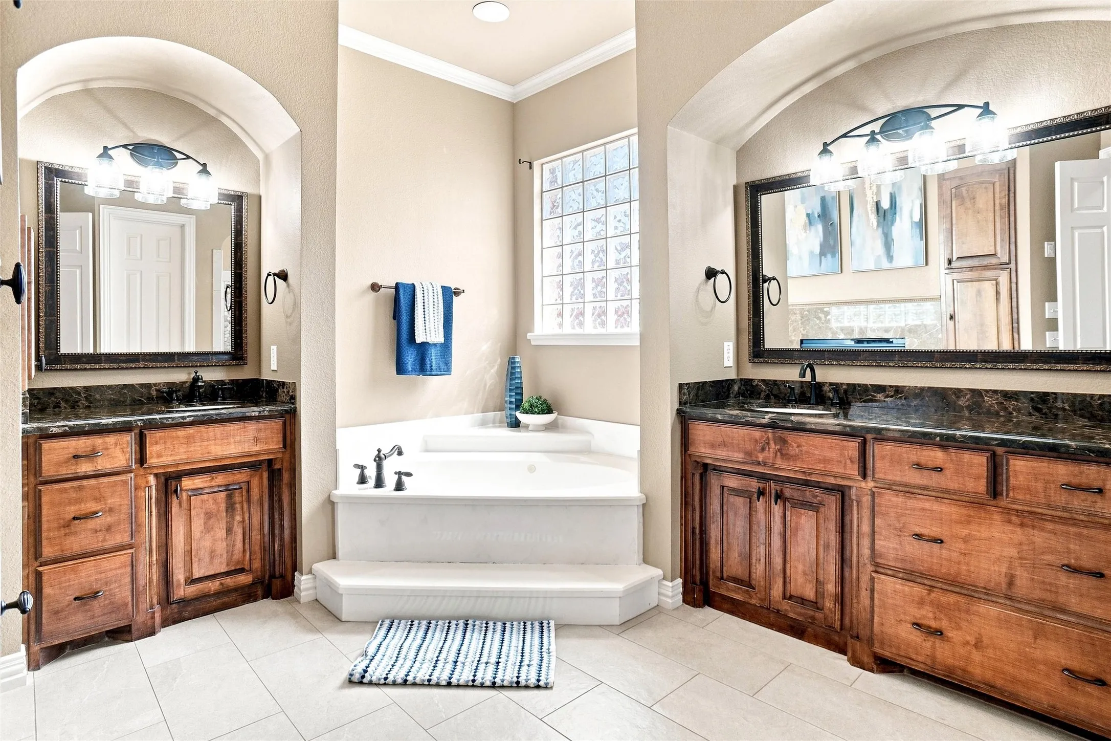 Dual vanity areas with dark stone countertops, wood cabinetry, and framed mirrors