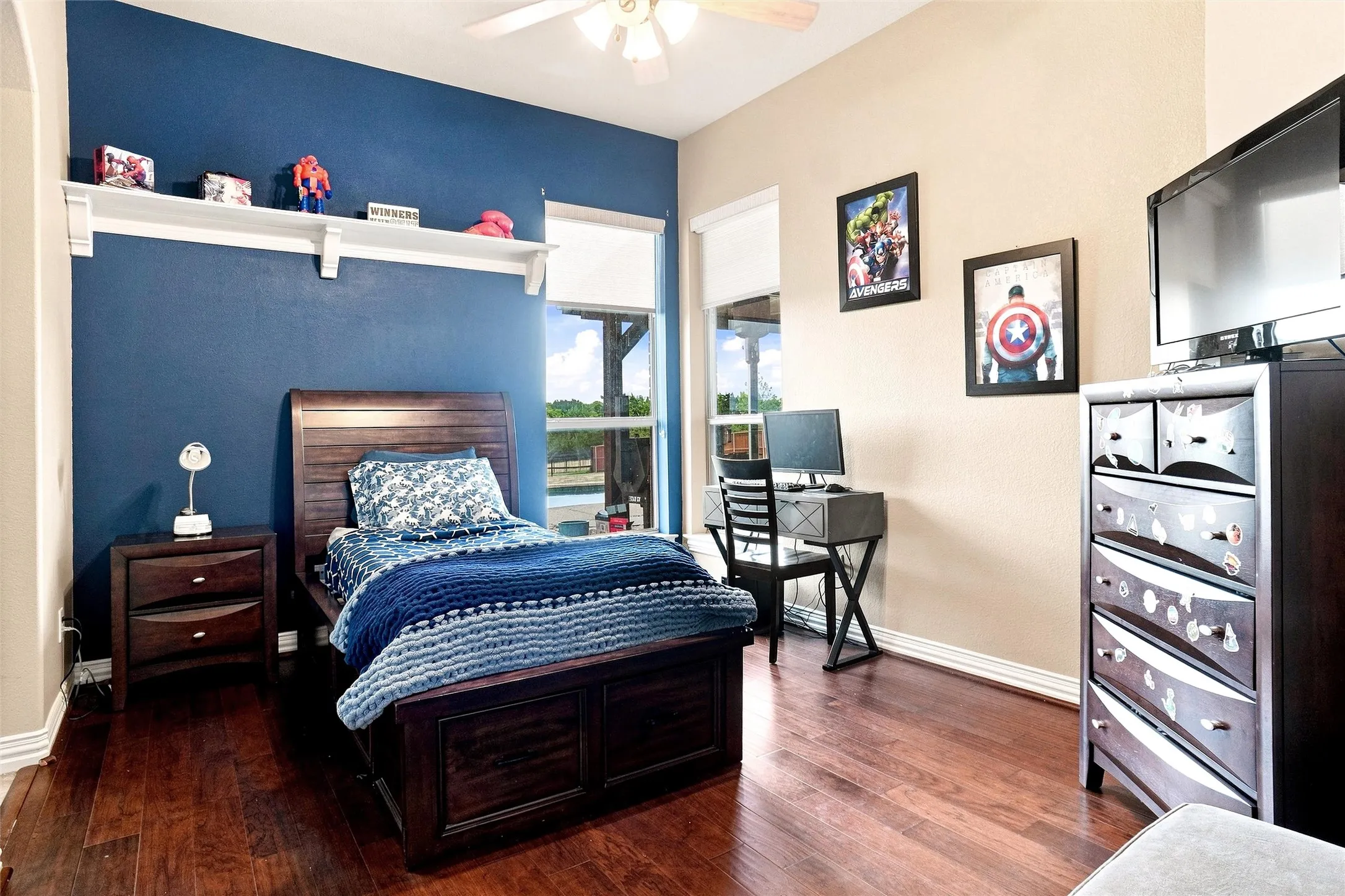 Wood-finish flooring throughout, ceiling fan with light fixture, built-in wall shelf, and windows with roller shades