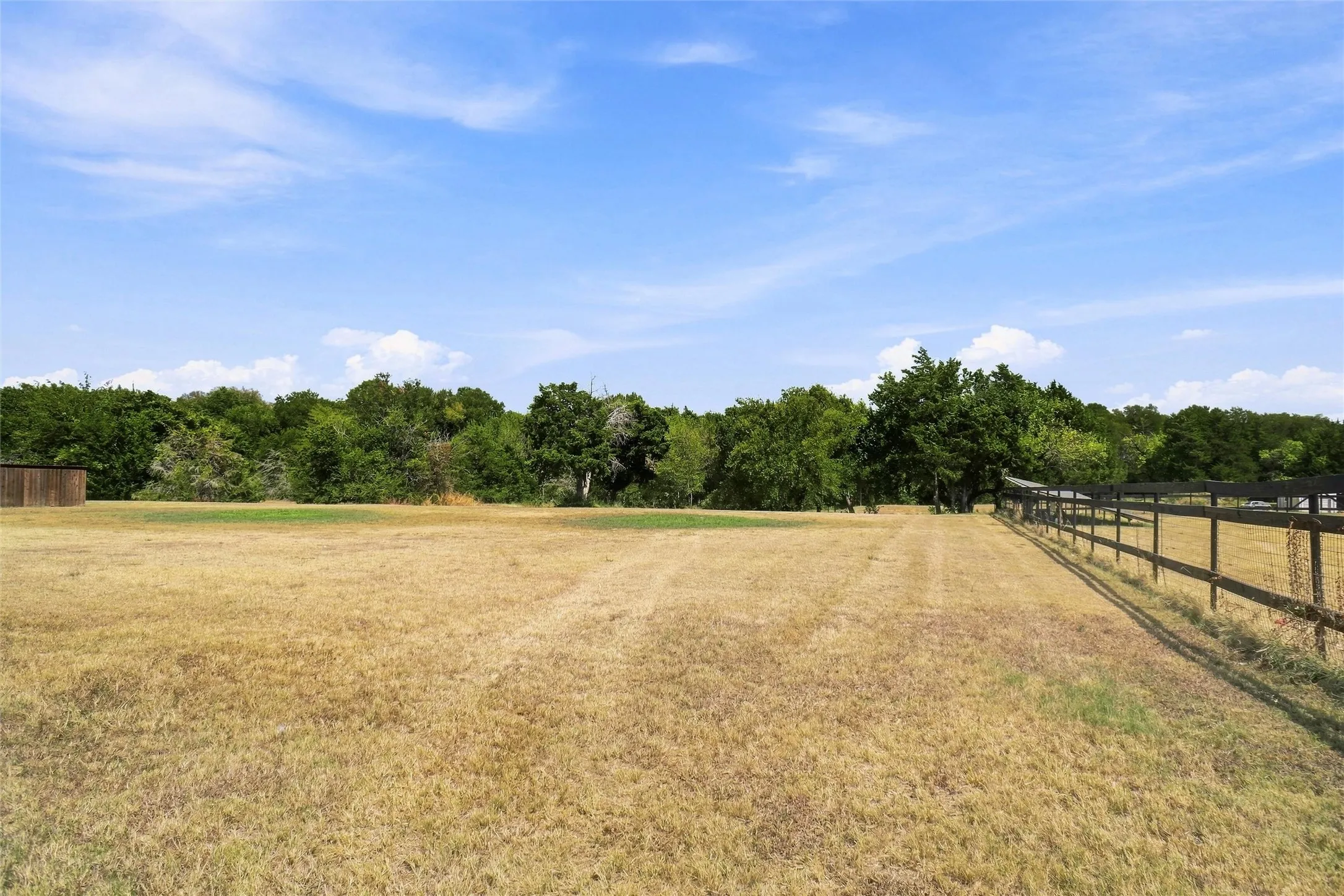 Expansive open field with a dark wood fence and dense tree line