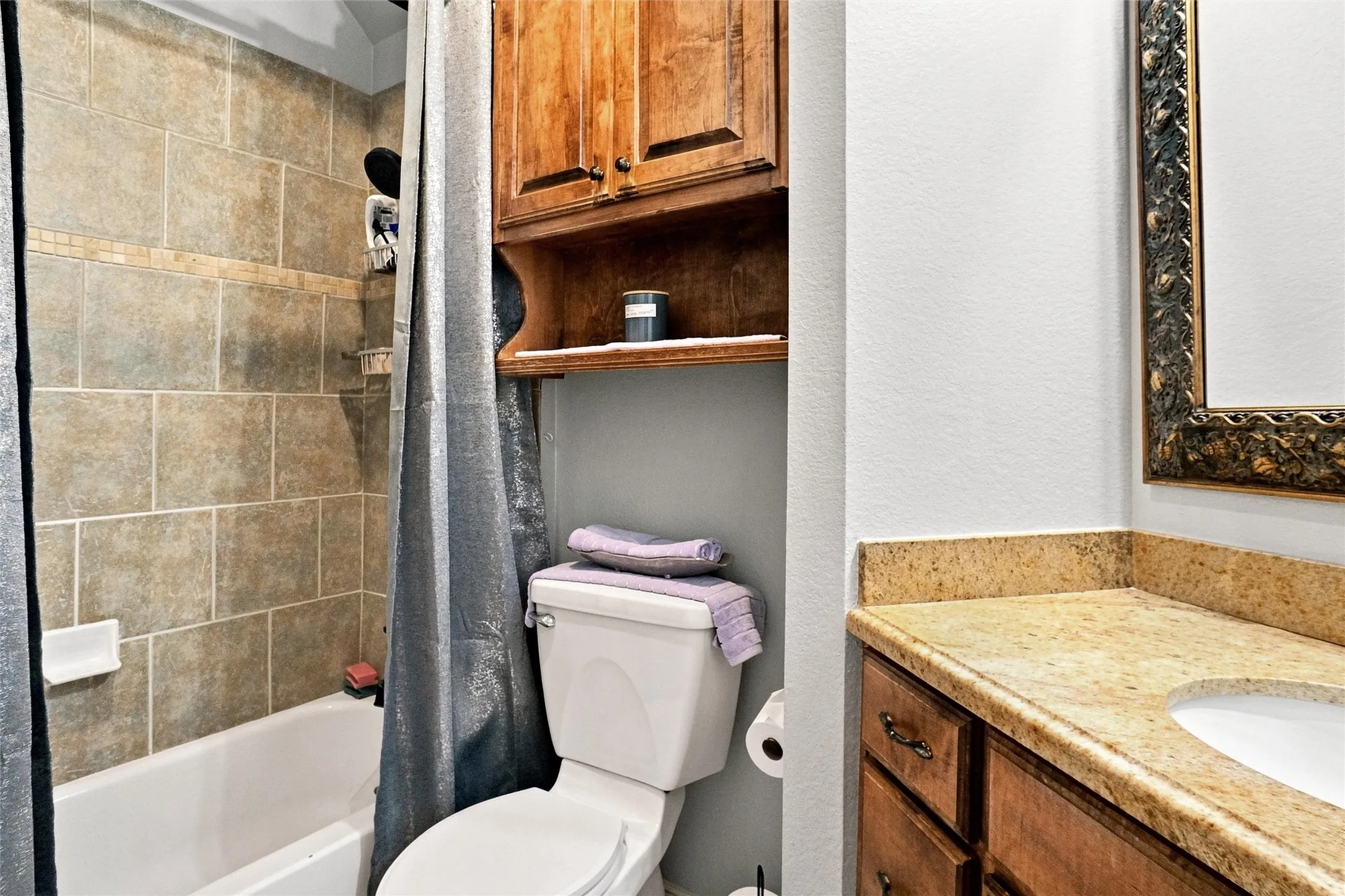 Bathtub with tiled surround, wood-finish vanity with an integrated sink, and an ornate framed mirror
