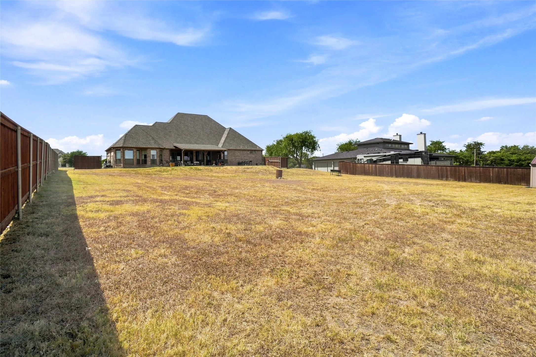 Expansive backyard with a wood privacy fence, featuring a large brick exterior home with a covered patio