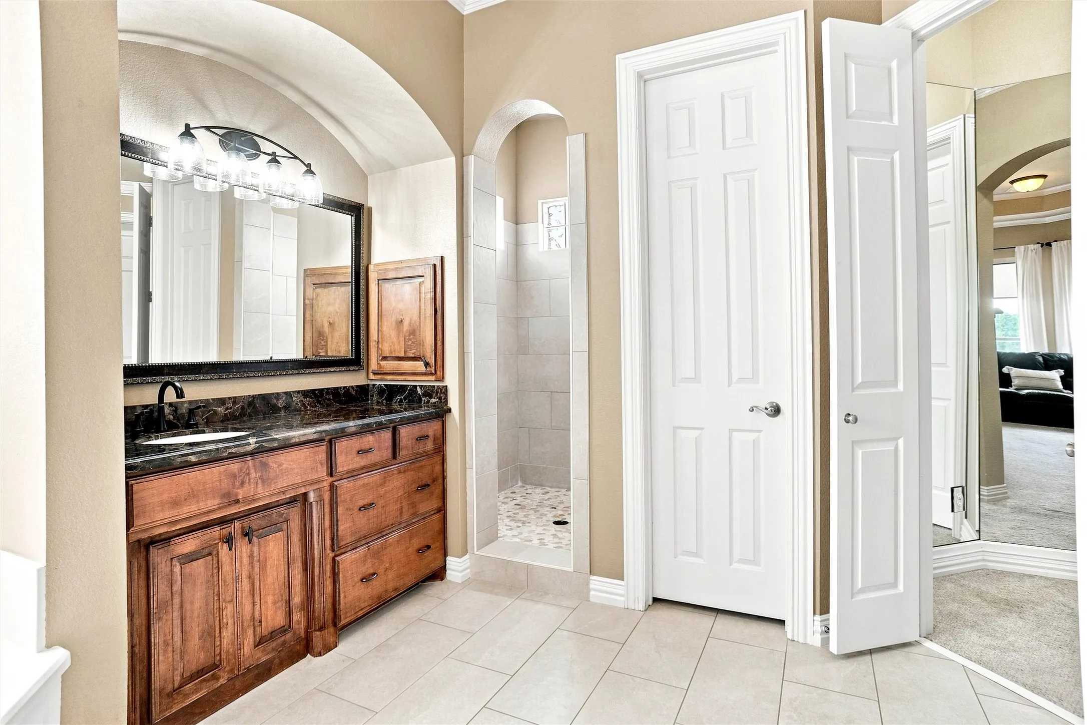 Bathroom featuring an arched entry, tile flooring, wood-finish vanity with dark countertop, built-in shower with tile surround, and a paneled interior door