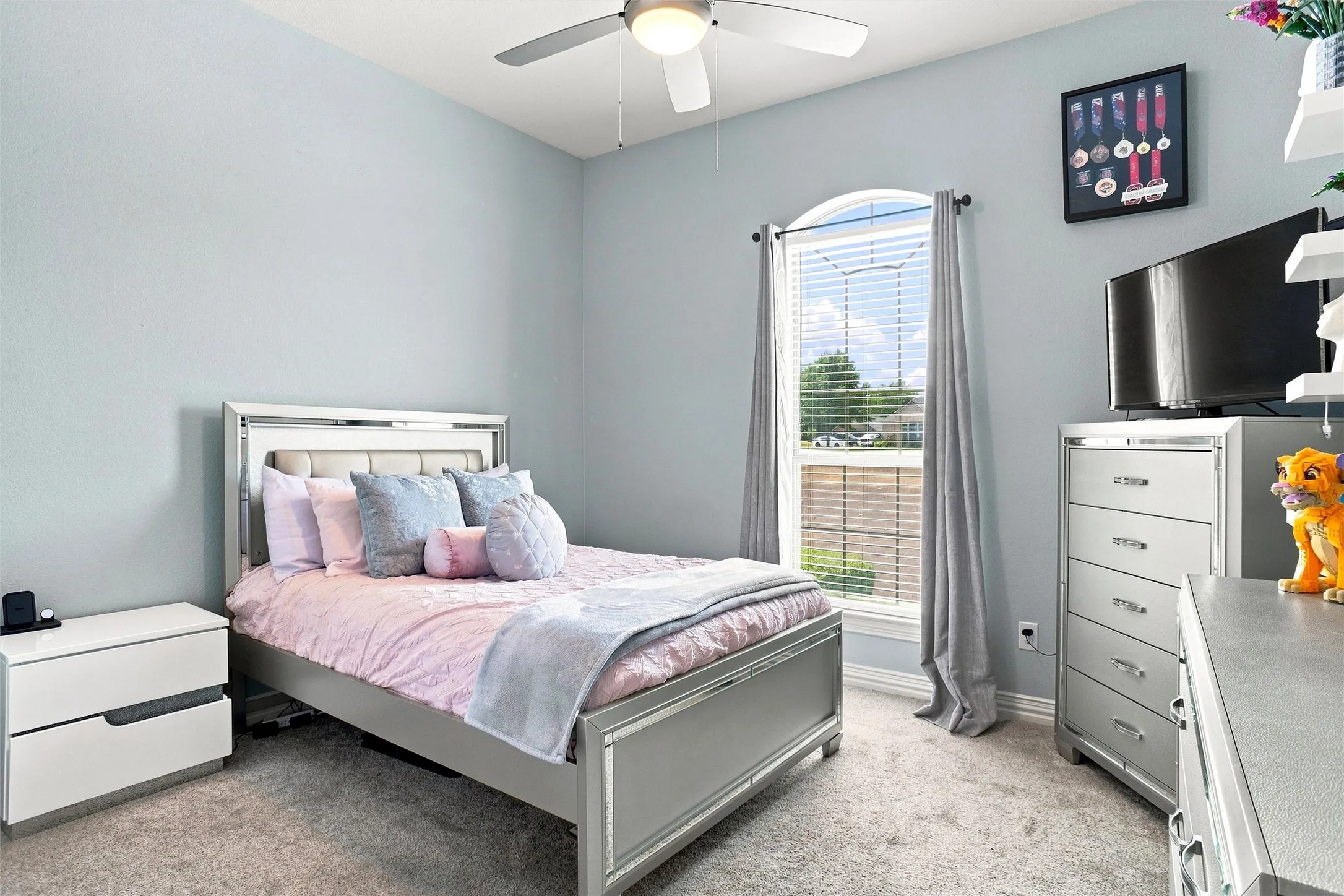 Arched window with blinds, ceiling fan, and light-toned carpet flooring