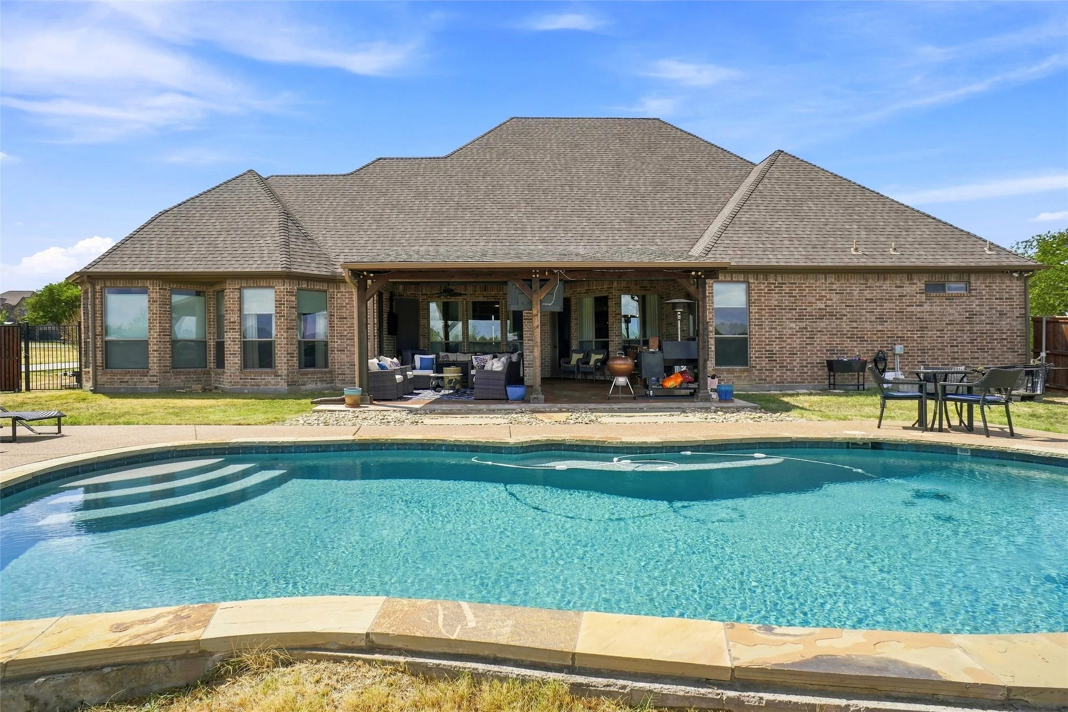 Brick exterior with multiple windows and a covered patio overlooking a swimming pool with integrated steps