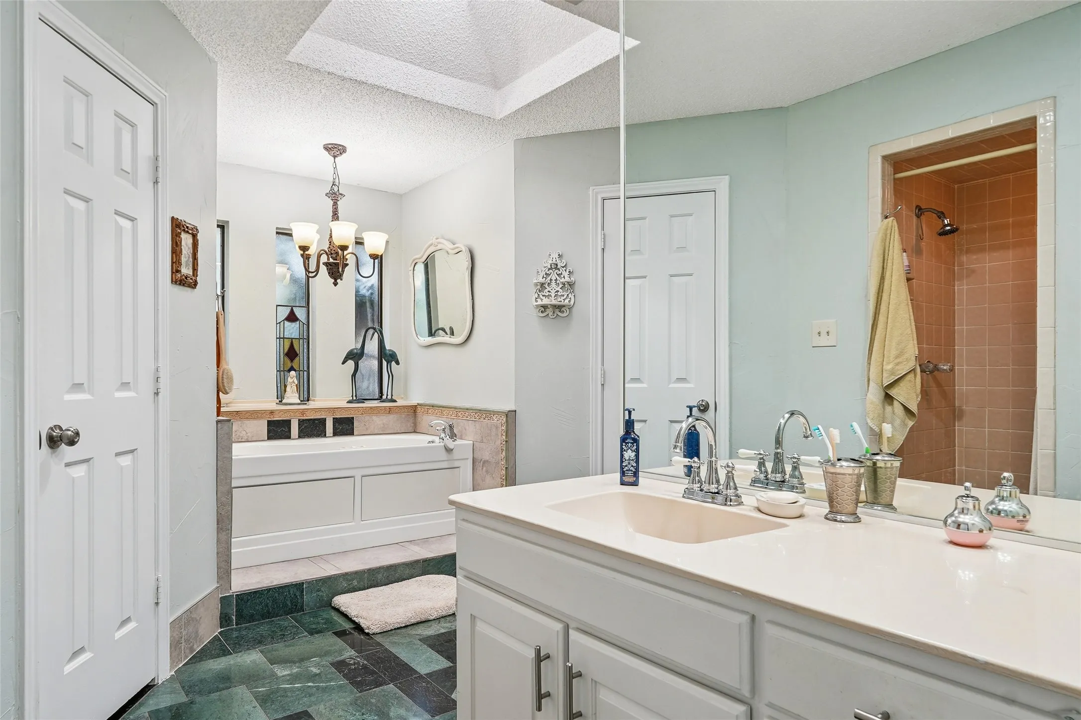Built-in soaking tub, vanity with integrated sink, overhead skylight, and tiled shower enclosure