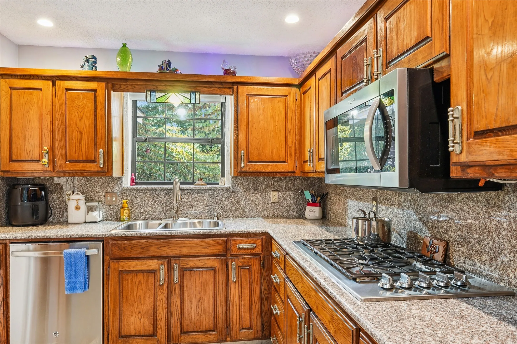 Wood-finish cabinetry, stainless steel appliances, dual basin sink, and a built-in gas cooktop
