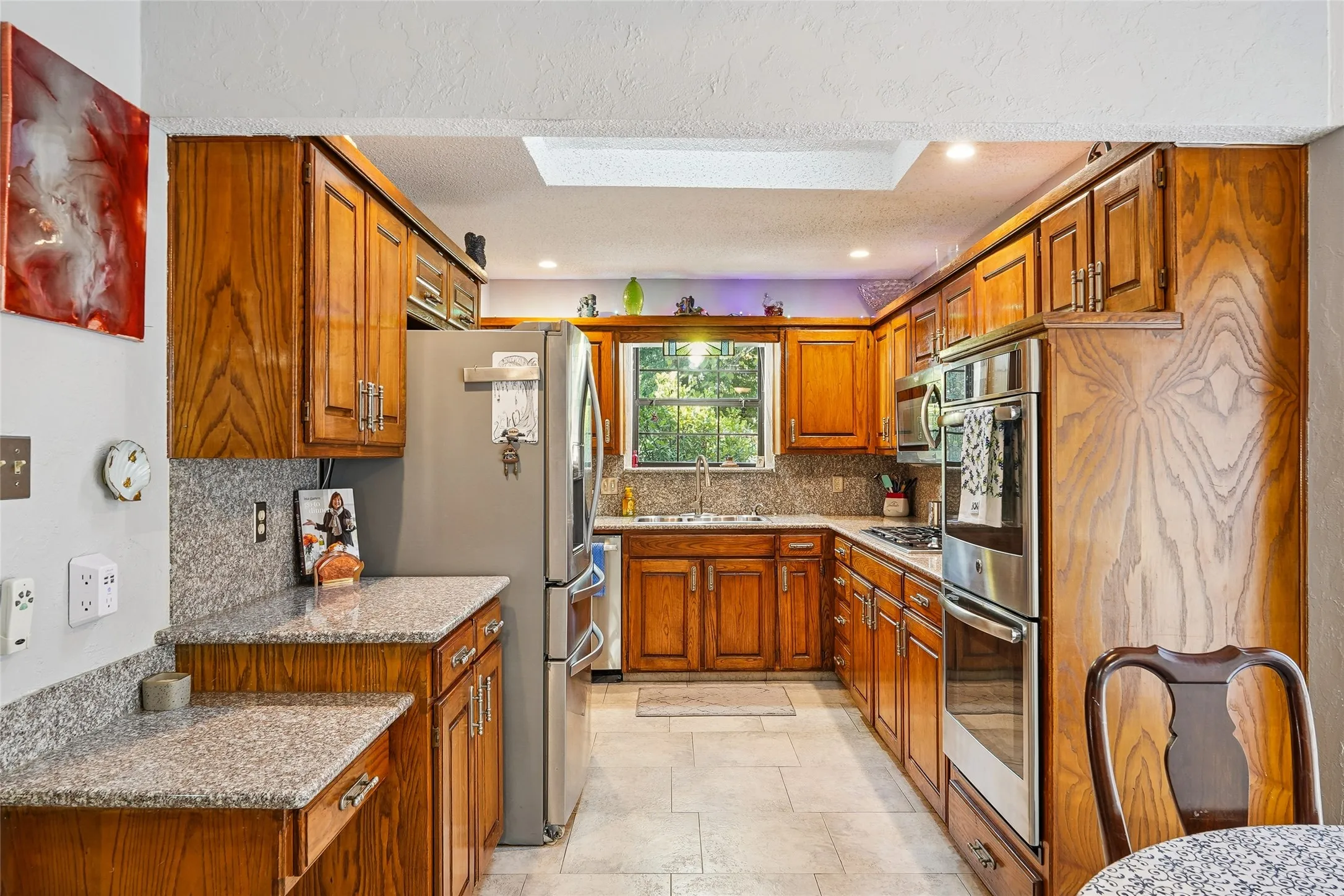 U-shaped kitchen with wood cabinetry, light-toned granite countertops and backsplash, stainless steel appliances, and recessed lighting