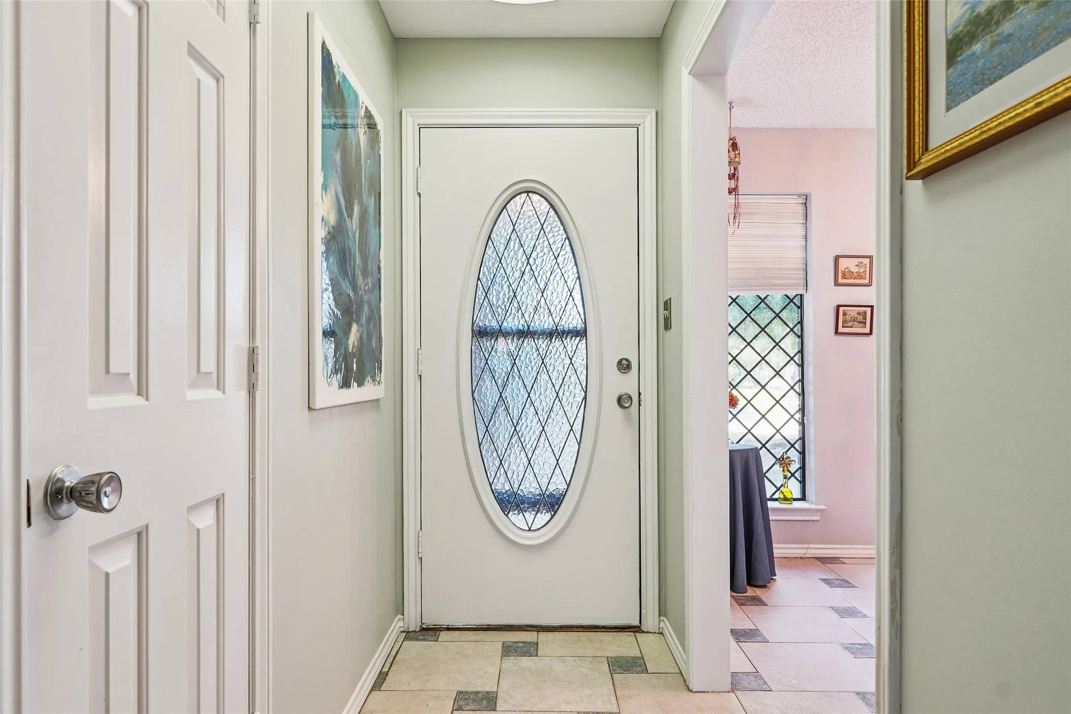 Entry door with an oval-leaded glass insert, light-toned wall paint, and multi-tone square tile flooring