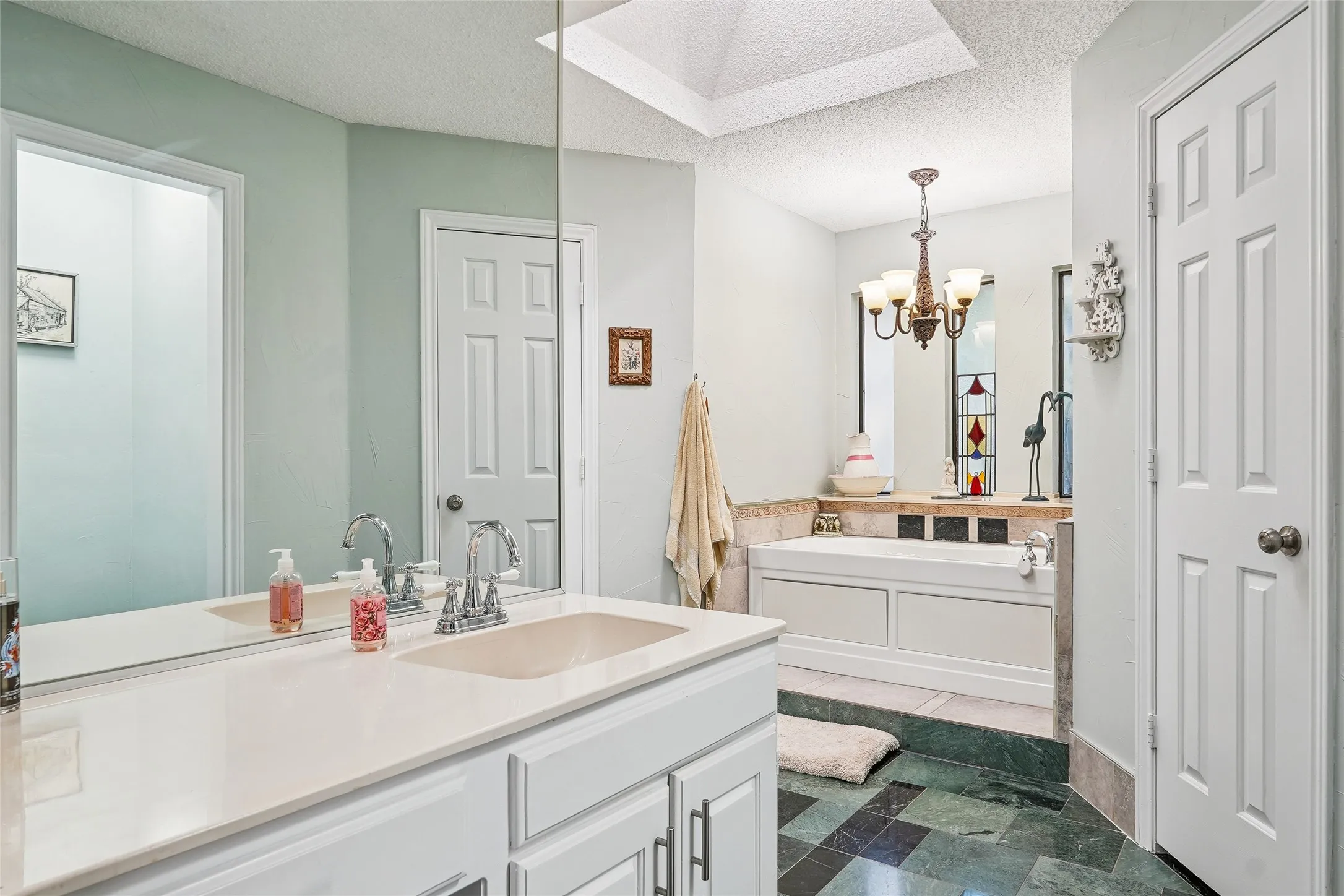Bathroom featuring a single vanity, built-in tub, overhead chandelier, and patterned floor tile