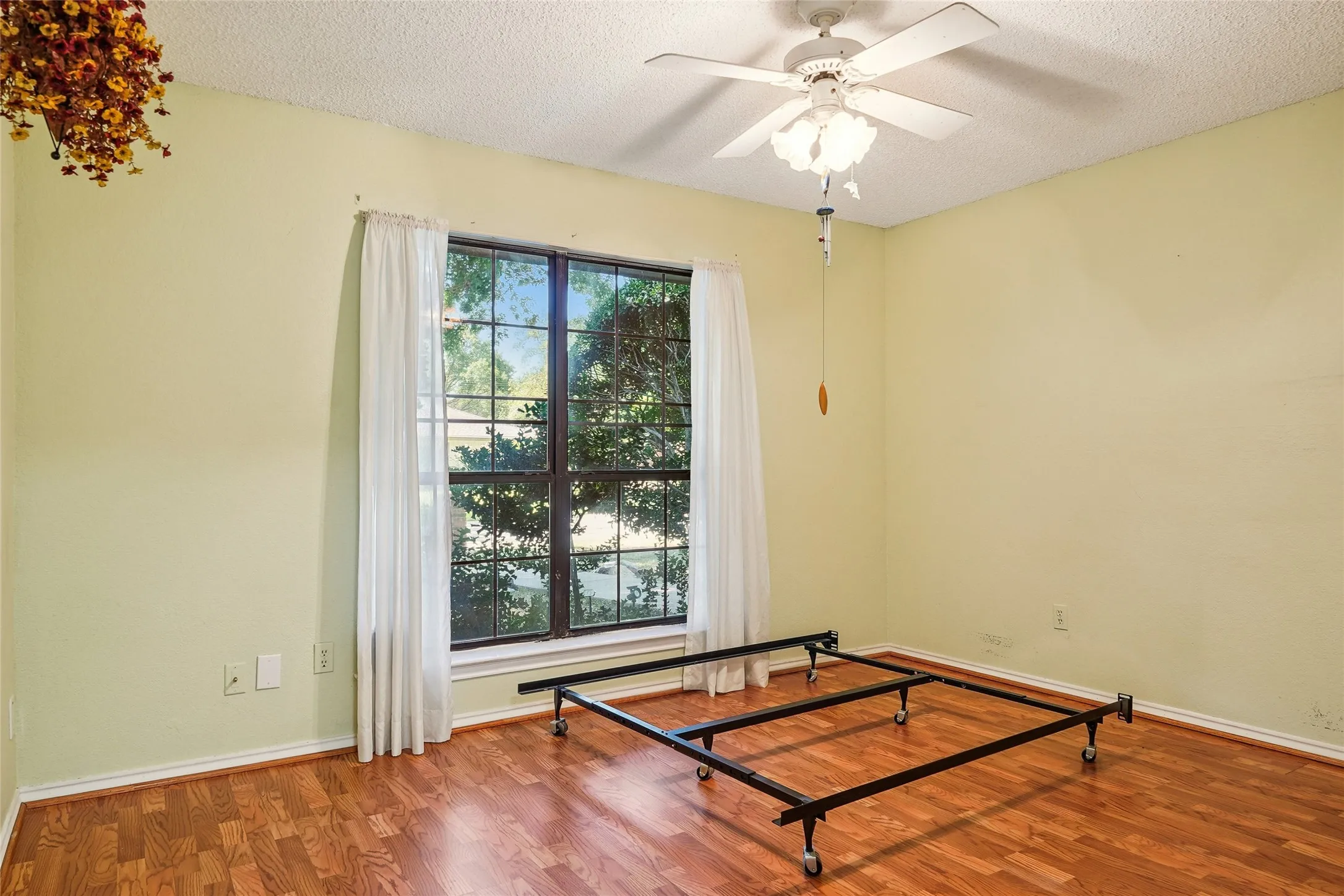 Wood-finish flooring, central ceiling fan, and a large window providing natural illumination
