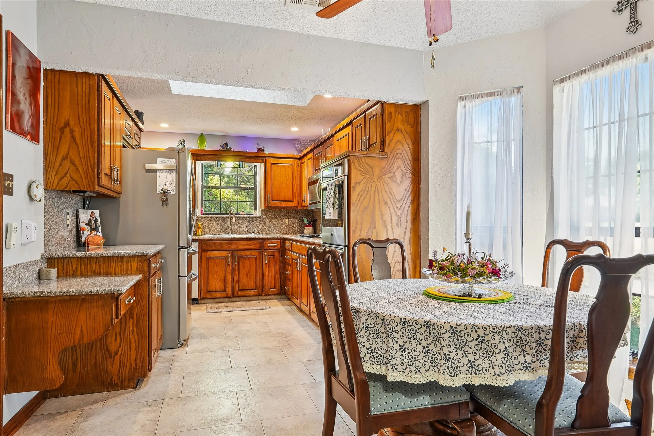 Kitchen featuring wood-finish cabinetry, light-colored tile flooring, built-in stainless steel appliances, and a skylight