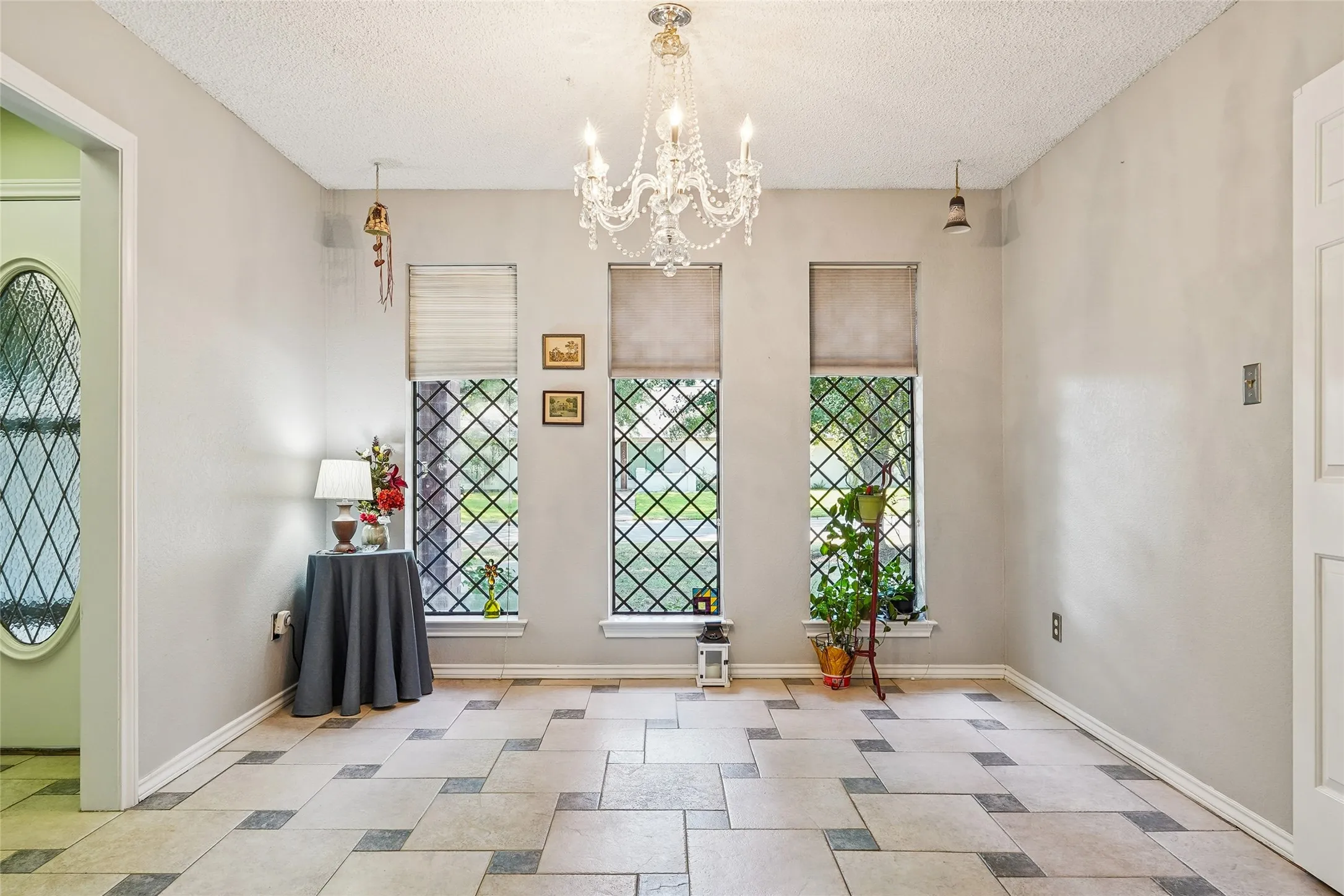 Recessed lighting, chandelier, three windows with decorative grilles, and tile flooring with a patterned inlay