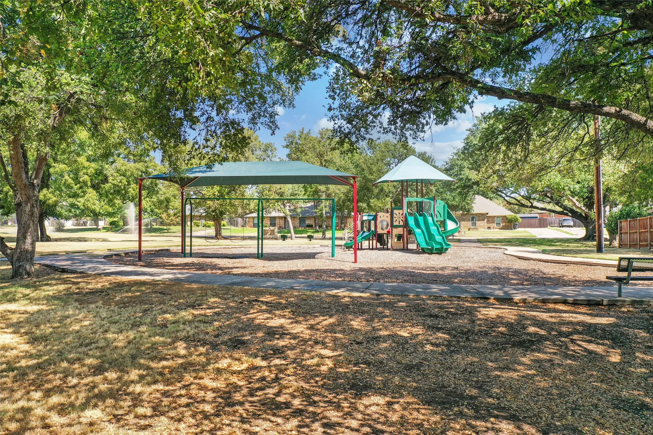 Shaded playground structure featuring multiple slides and an additional covered swing set area