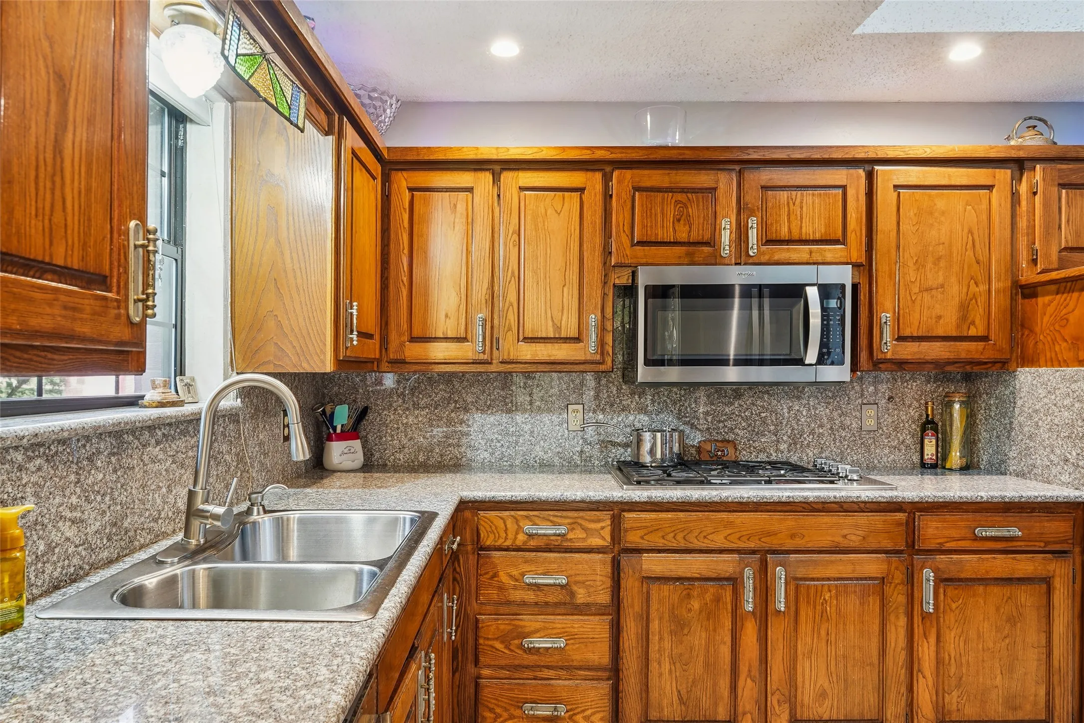 Kitchen featuring wood cabinetry, light-toned countertops, a built-in stainless steel microwave, and a gas cooktop