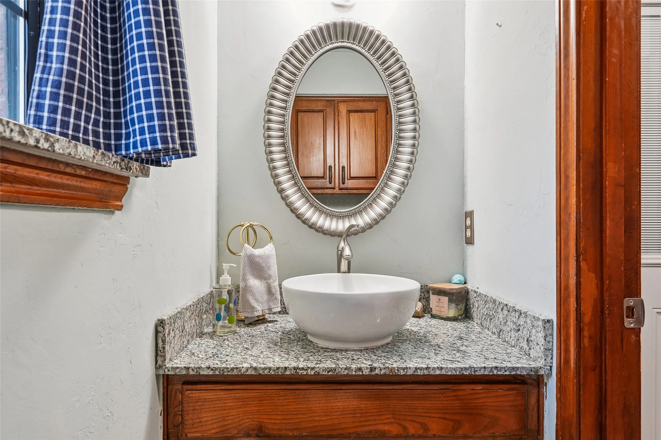 Granite countertop, vessel sink, polished chrome faucet, wood-finish vanity, and an ornate oval mirror