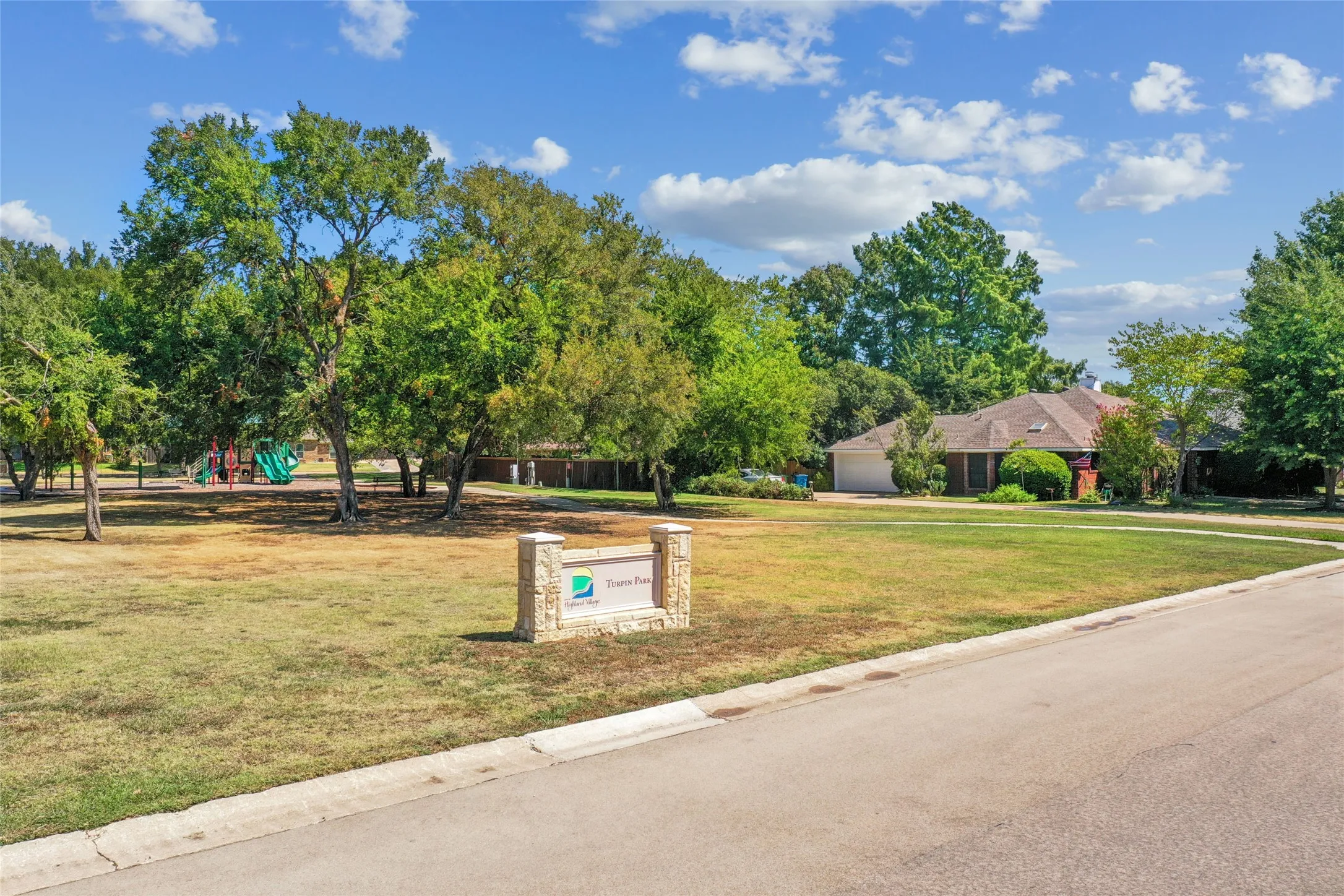 Neighborhood park with mature trees, expansive green space, and a stone-clad entry monument