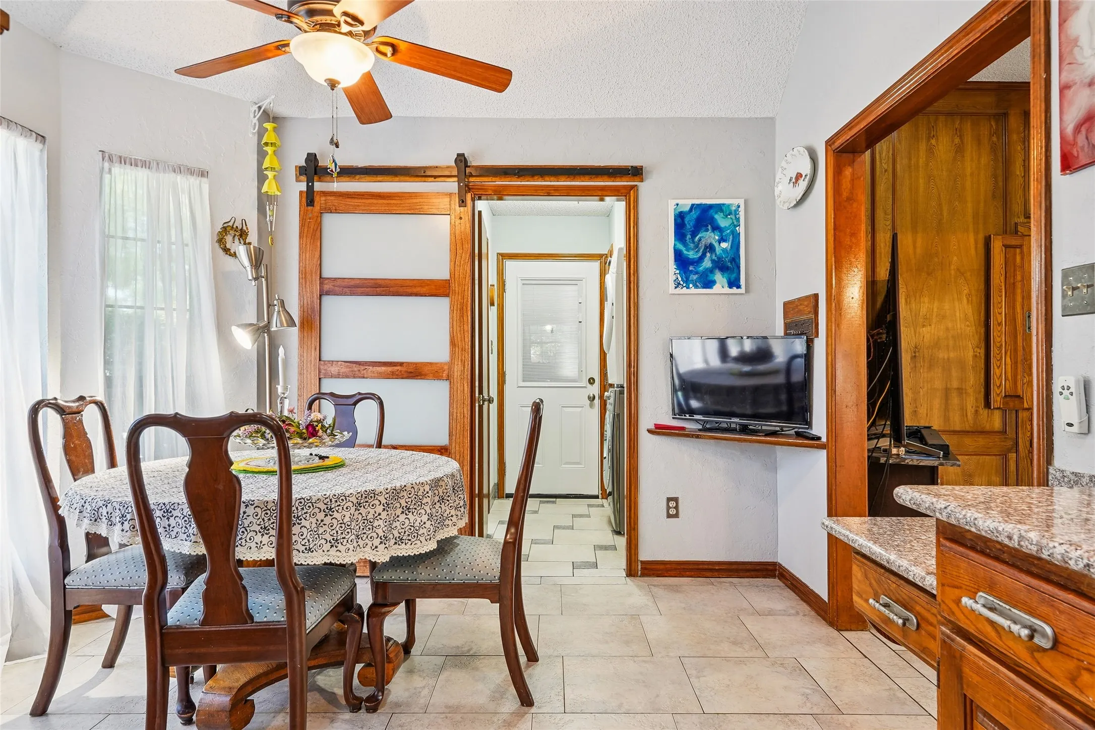Tile flooring, wood-finish ceiling fan, wood-finish trim, sliding barn door with frosted panels, and granite-look countertop