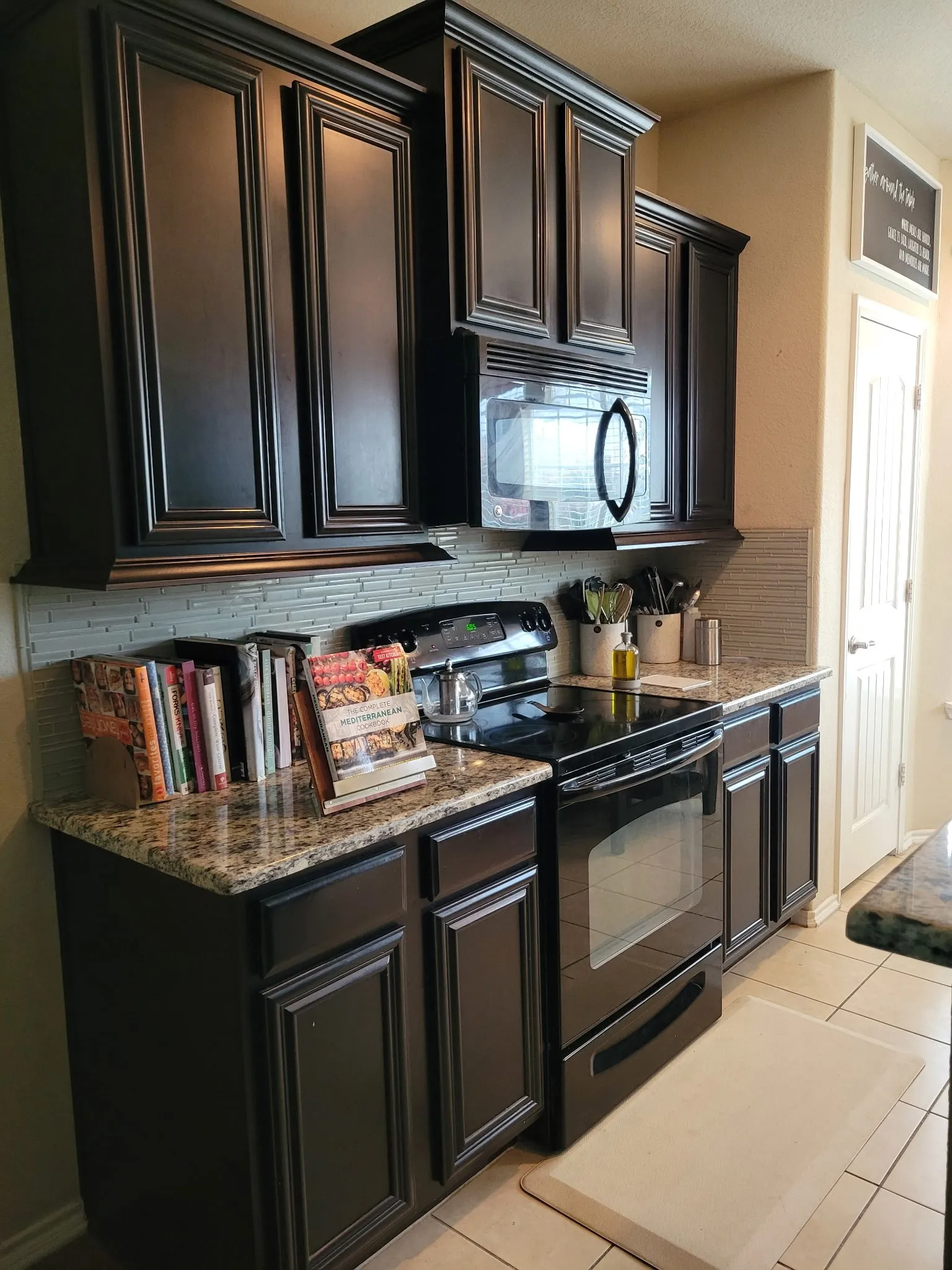 Dark wood-finish cabinetry with crown molding, granite-finish countertops, tiled backsplash, and built-in microwave