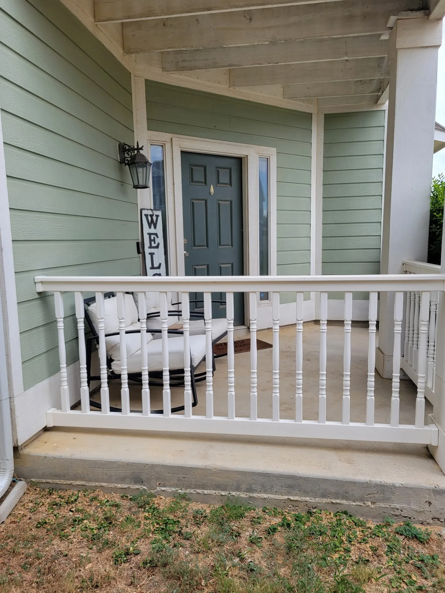 Covered porch featuring light green siding, white railing, and a dark-paneled entry door with sidelights