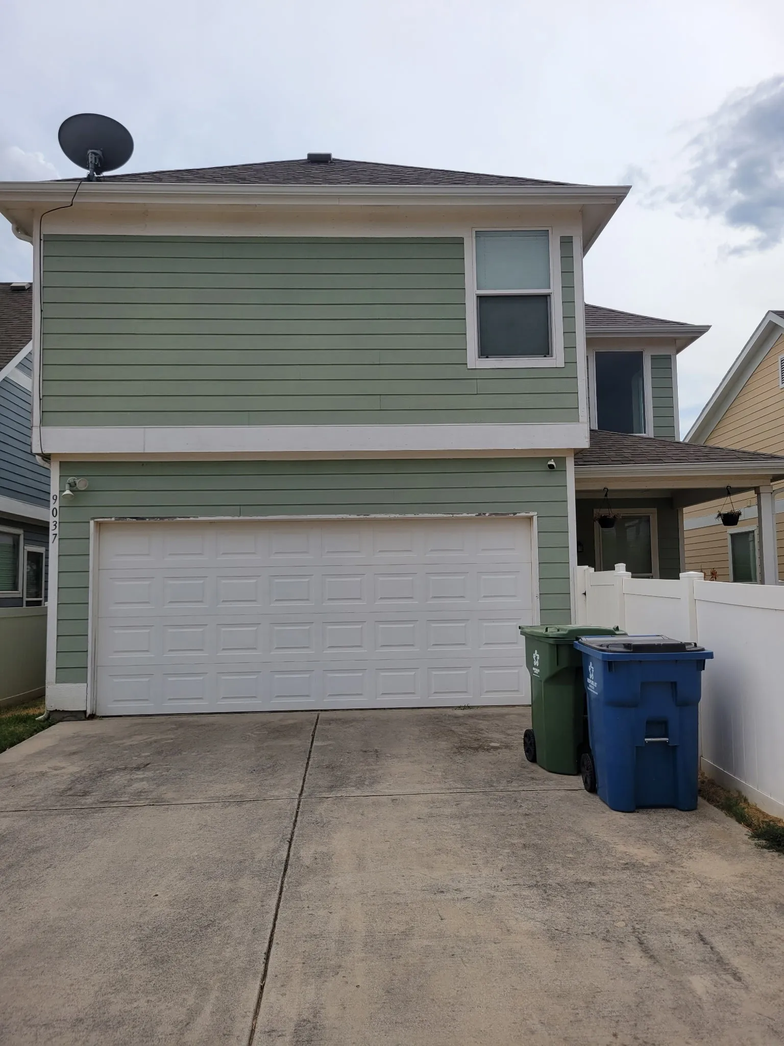 Two-story exterior with horizontal siding, featuring a two-car garage with a panel door, and a white privacy fence