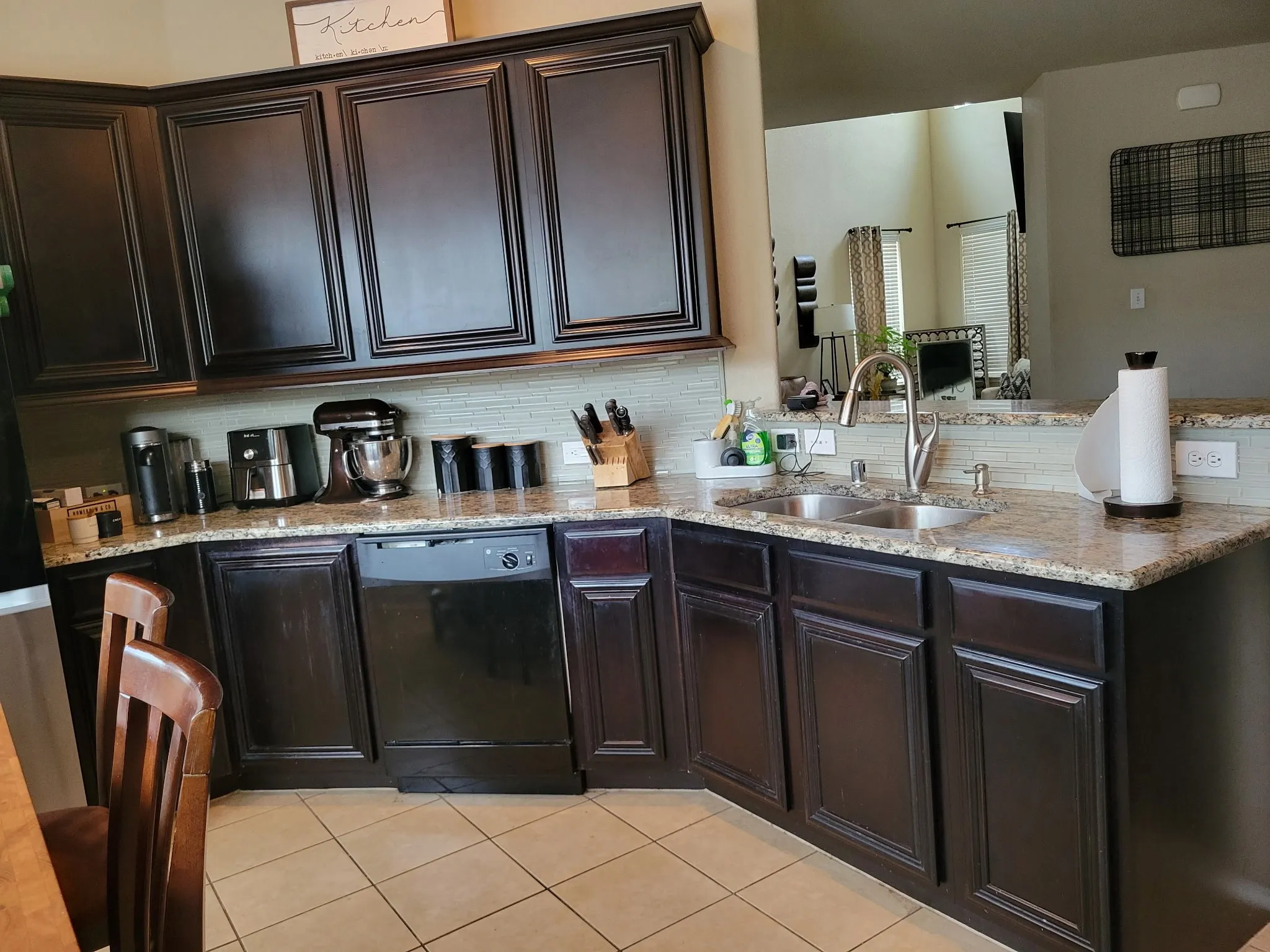 Dark wood-finish cabinetry, granite countertops, dual basin stainless steel sink, and a tiled backsplash
