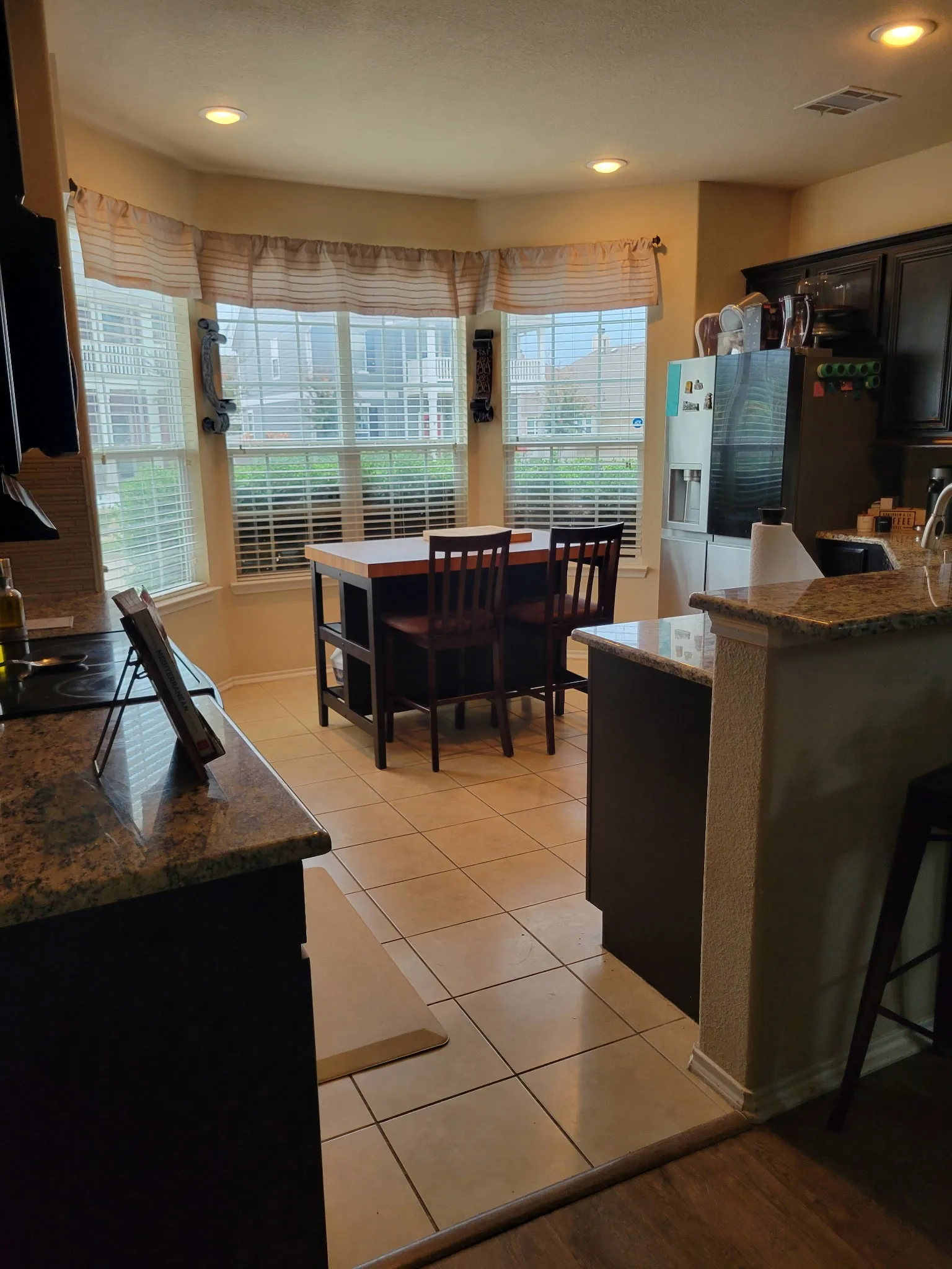 Bay window with multiple panes, recessed lighting, tile flooring, granite countertops, and dark wood-finish cabinetry