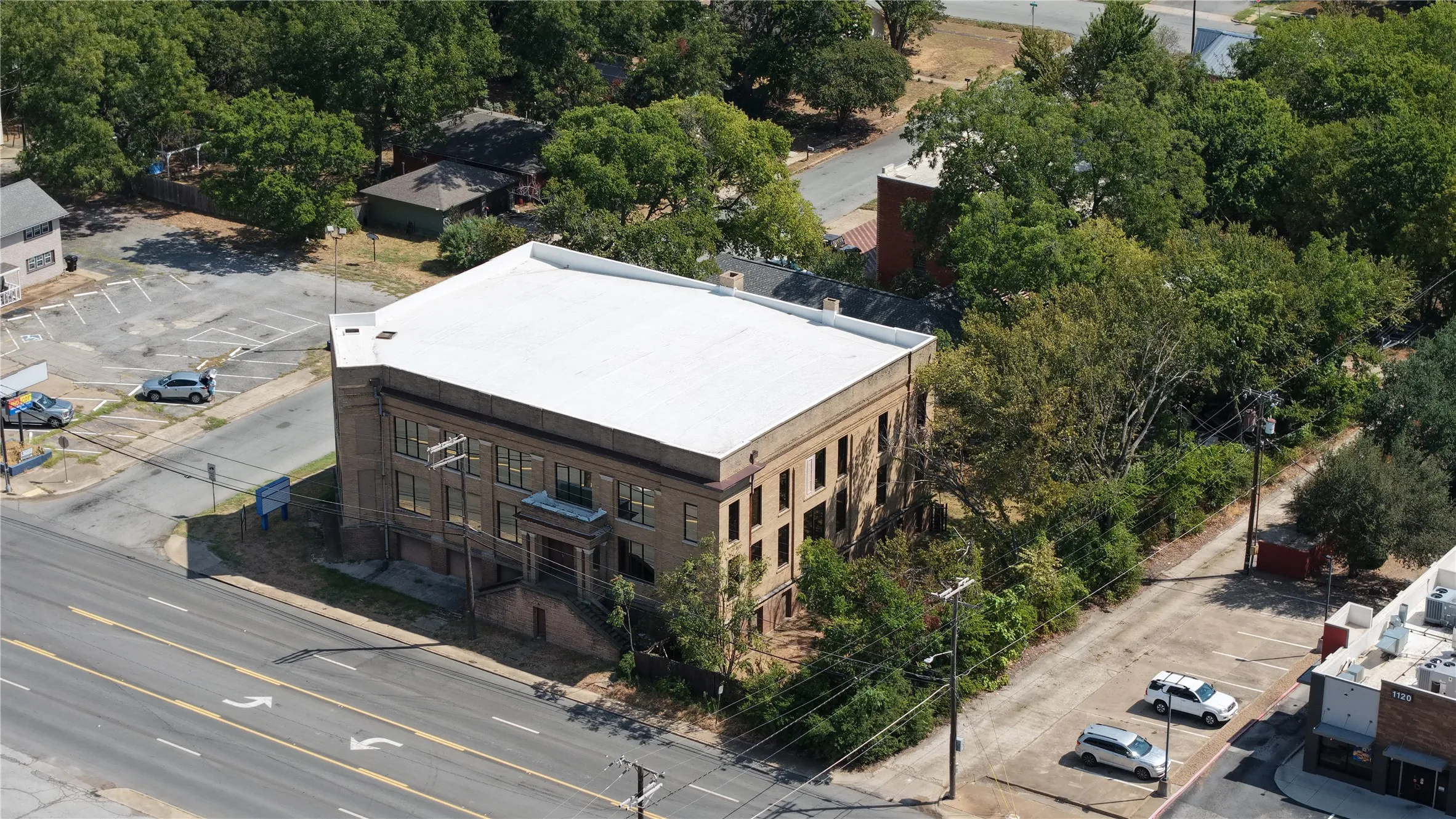 Multi-story commercial building with a light-colored roof, surrounded by mature trees