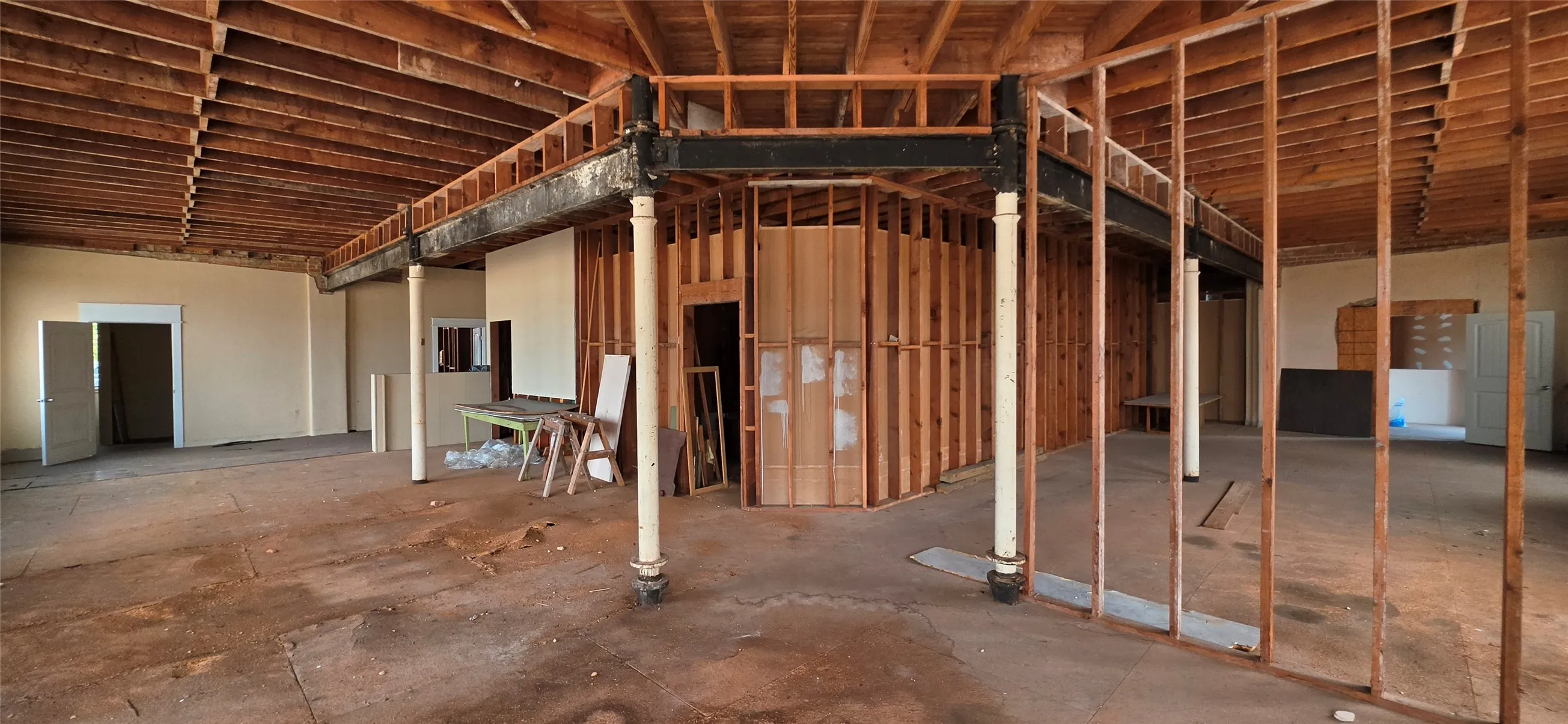 Exposed wood ceiling joists with steel support beams, framing for multiple rooms, and a large open floor area