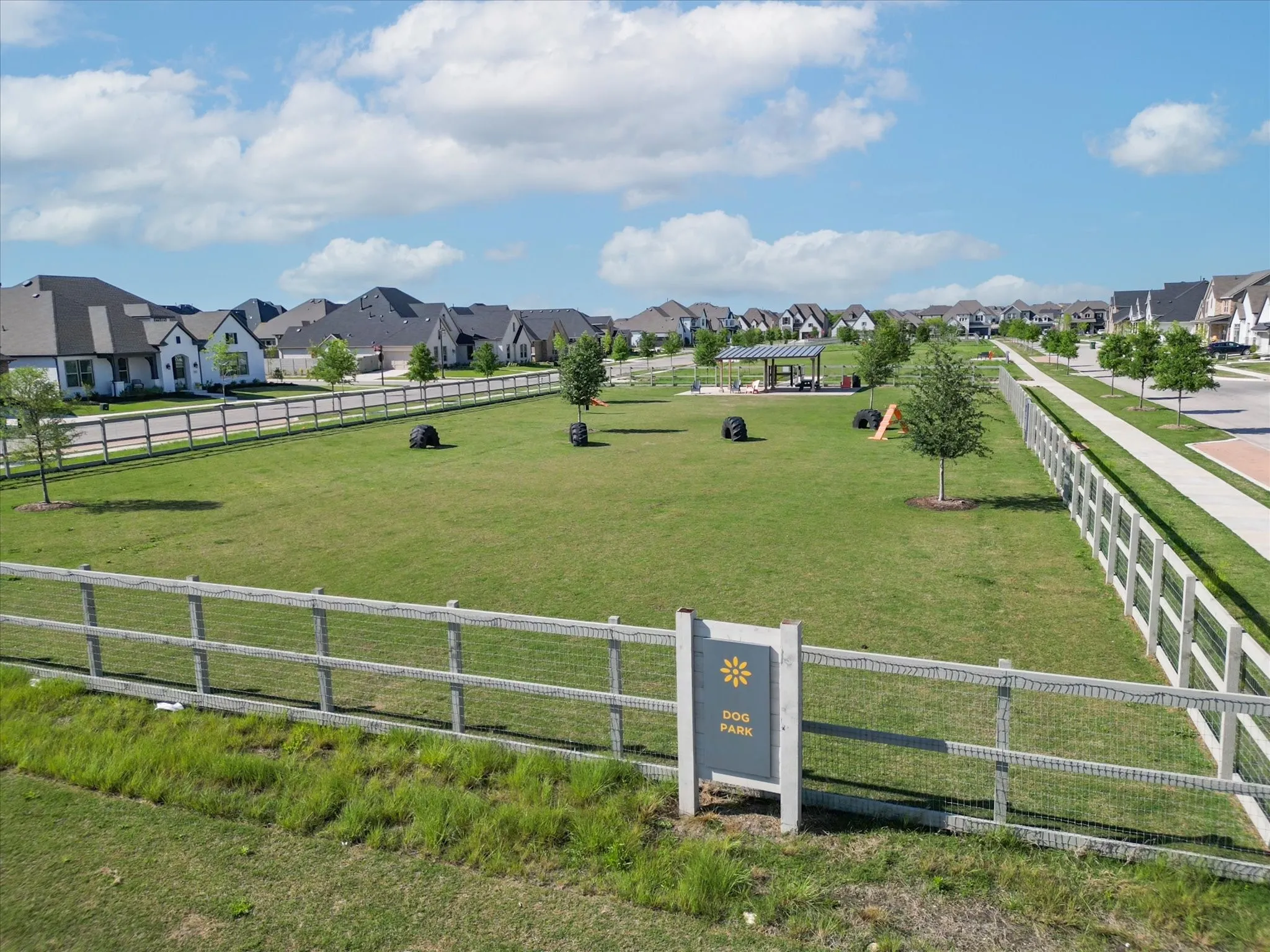 Expansive green space featuring a fenced dog park, covered pavilion, and walking paths, surrounded by residential properties