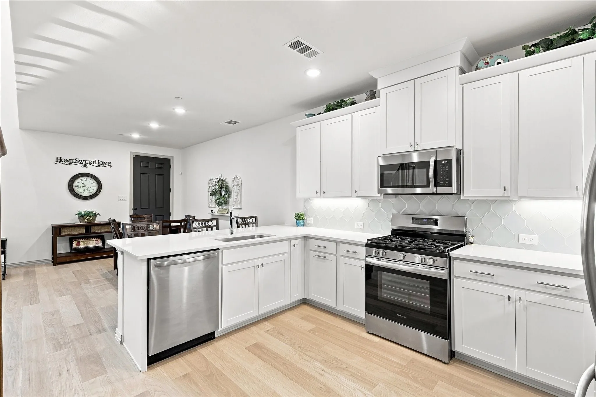 Modern kitchen featuring white cabinetry, stainless steel appliances, light wood-finish flooring, a tile backsplash, and recessed lighting