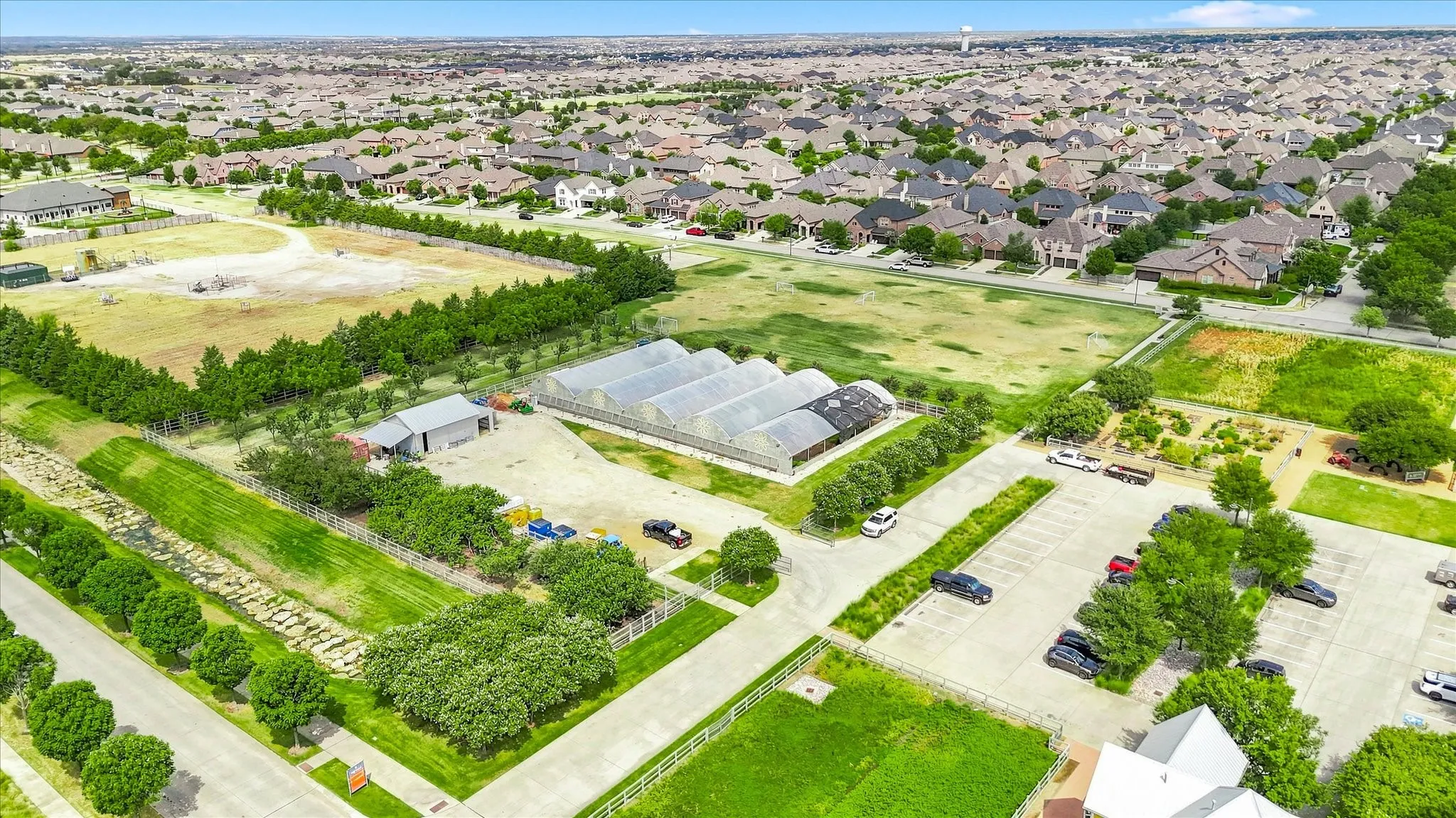 Expansive property featuring multiple greenhouses, a large parking area, and a utility building, surrounded by green spaces and mature trees
