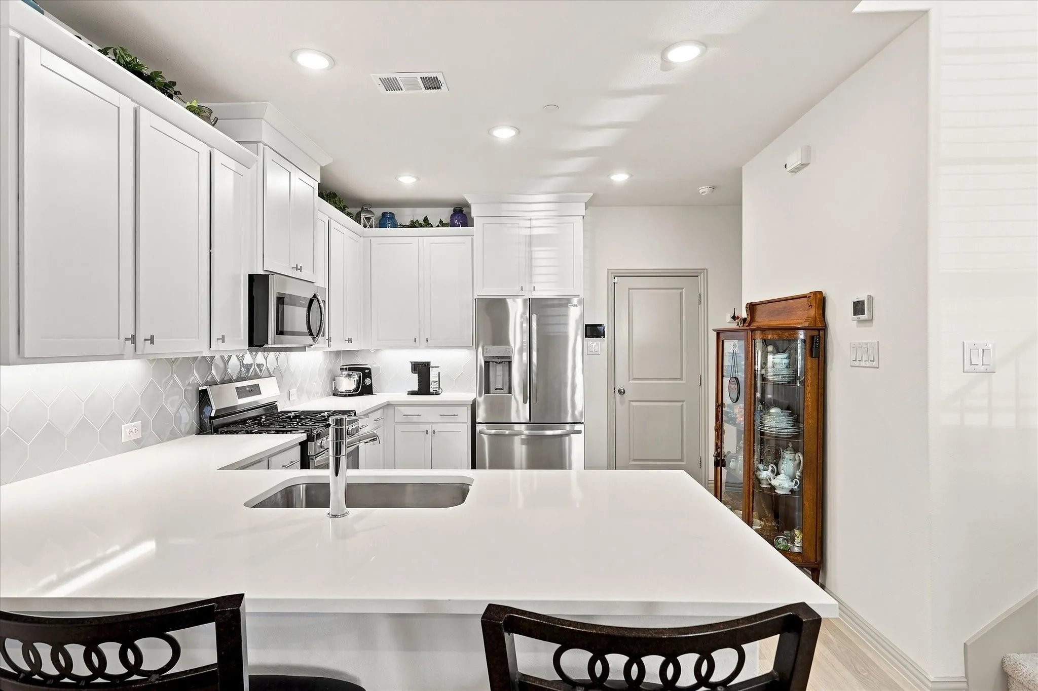 U-shaped kitchen featuring white cabinetry, light-toned countertops, a stainless steel sink with a gooseneck faucet, and integrated stainless steel appliances