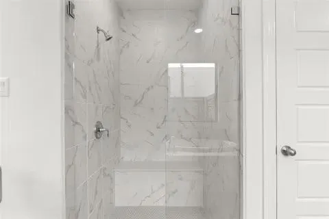Walk-in shower with clear glass enclosure and marble-patterned tile