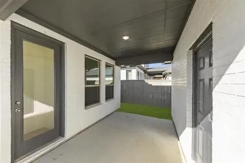 Covered patio with a concrete surface, white brick exterior, dark-framed windows, and a dark privacy fence