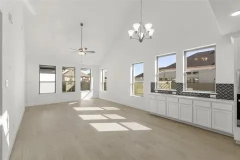 Vaulted ceiling, wood-finish flooring, white cabinetry, dark tile backsplash, and multiple windows