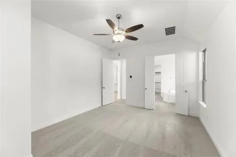 Vaulted ceiling with an attached ceiling fan, neutral carpet flooring, and a window for natural illumination