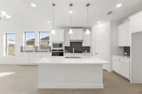 White cabinetry, an expansive kitchen island, recessed lighting, pendant lighting, and dark tile backsplash
