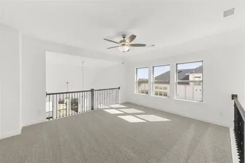 Open loft area featuring three windows, a ceiling fan, and carpeted flooring