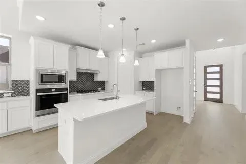 White kitchen cabinetry, stainless steel appliances, solid surface countertops, a center island with a sink, and wood-finish flooring