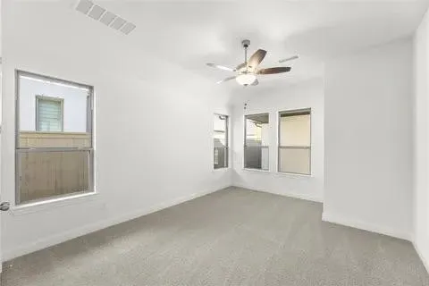 Neutral color palette with light gray carpeting, multiple windows, and a ceiling fan with integrated lighting