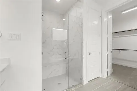 Frameless glass shower enclosure with tiled walls, built-in shower bench, recessed lighting, and grey tile flooring